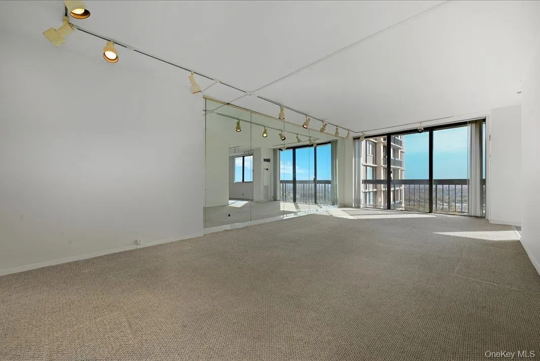 Carpeted empty room with track lighting and expansive windows Carpeted empty room with track lighting and expansive windows