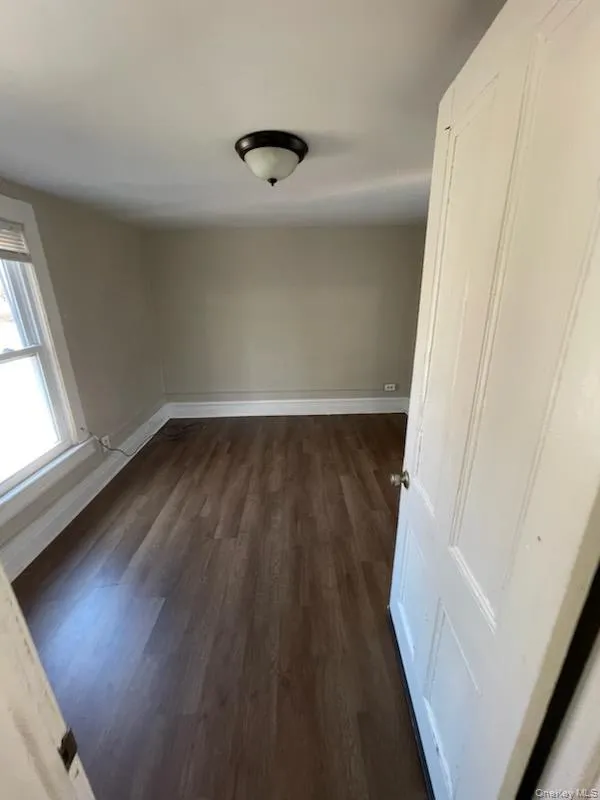 Spare room featuring baseboards and dark wood-style floors Spare room featuring baseboards and dark wood-style floors