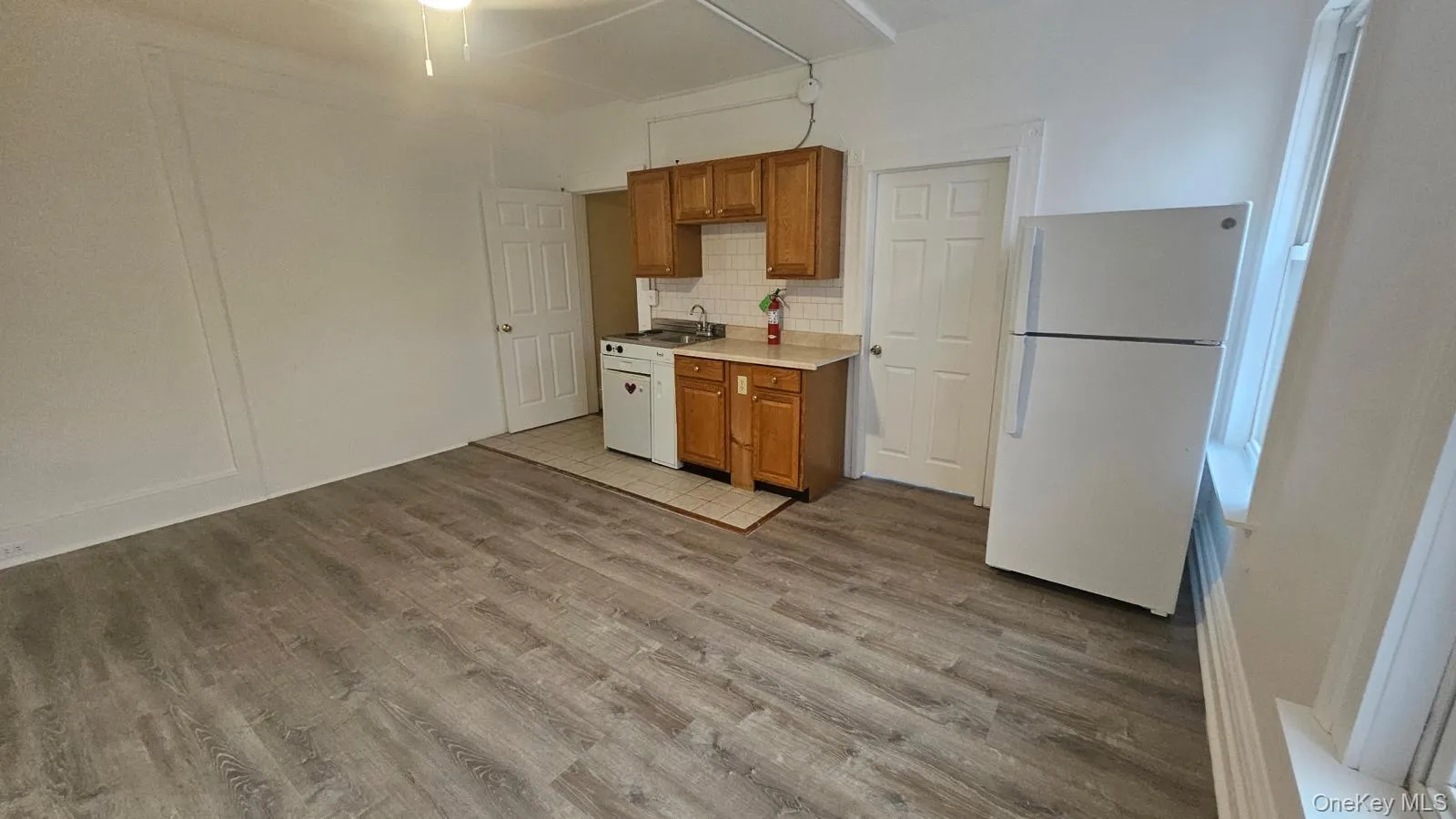 Kitchen featuring light countertops, brown cabinetry, freestanding refrigerator, decorative backsplash, and light wood-type flooring Kitchen featuring light countertops, brown cabinetry, freestanding refrigerator, decorative backsplash, and light wood-type flooring