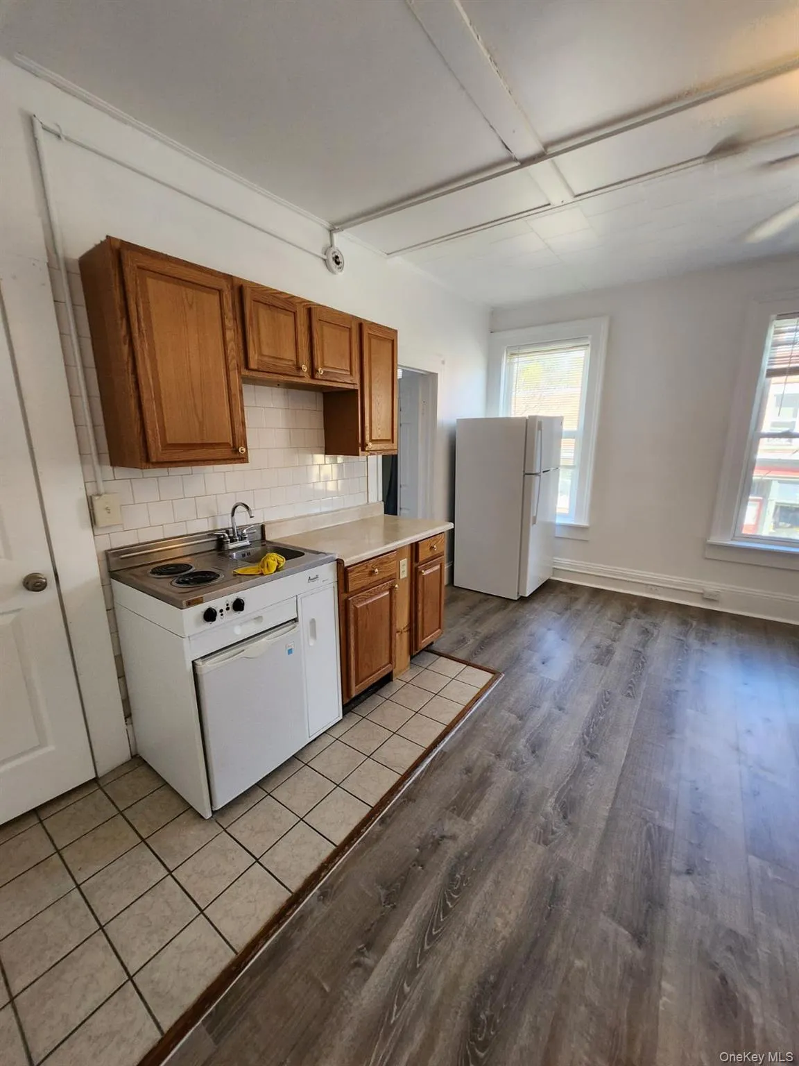 Kitchen with brown cabinetry, backsplash, white appliances, dark tile patterned floors, and light countertops Kitchen with brown cabinetry, backsplash, white appliances, dark tile patterned floors, and light countertops