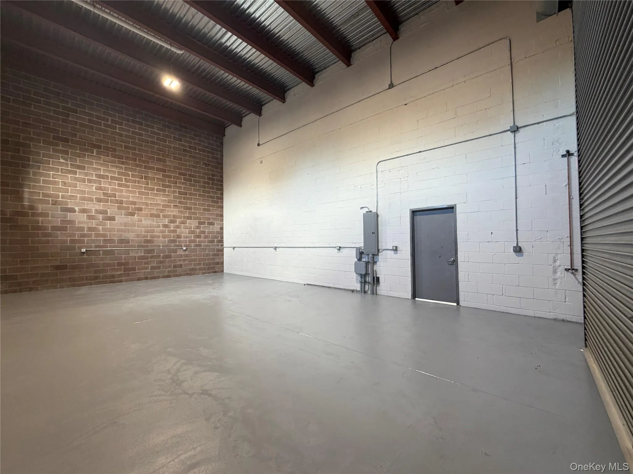 Miscellaneous room featuring concrete flooring, a towering ceiling, brick wall, and electric panel Miscellaneous room featuring concrete flooring, a towering ceiling, brick wall, and electric panel