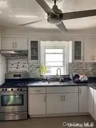 Kitchen with stainless steel gas range oven, glass insert cabinets, dark countertops, white cabinetry, and backsplash Kitchen with stainless steel gas range oven, glass insert cabinets, dark countertops, white cabinetry, and backsplash