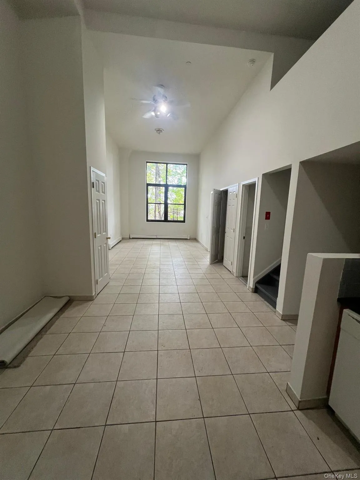Unfurnished room with light tile patterned flooring, stairway, a ceiling fan, and vaulted ceiling Unfurnished room with light tile patterned flooring, stairway, a ceiling fan, and vaulted ceiling