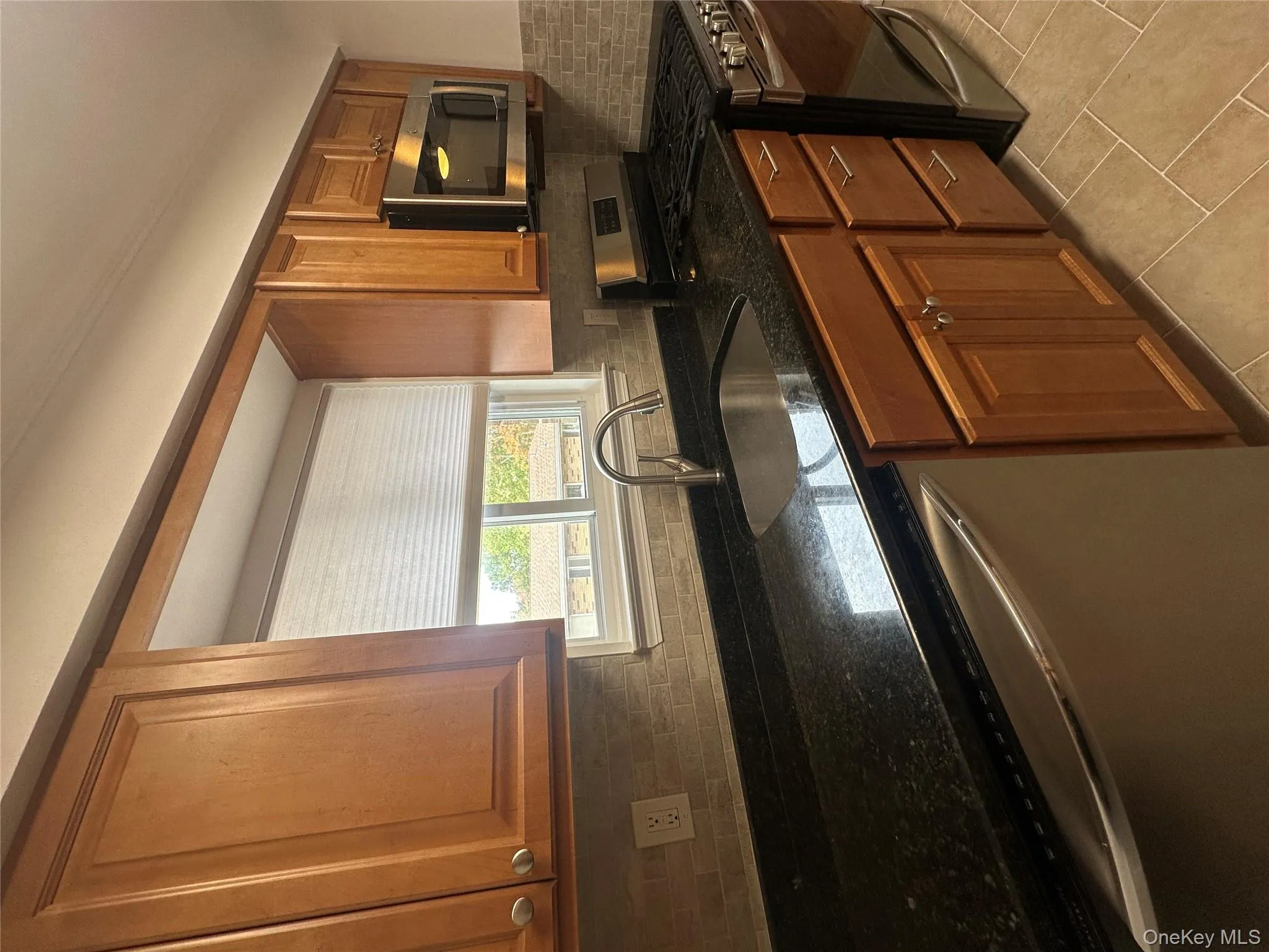 Kitchen with dishwashing machine, stainless steel range oven, brown cabinets, tasteful backsplash, and dark stone counters Kitchen with dishwashing machine, stainless steel range oven, brown cabinets, tasteful backsplash, and dark stone counters