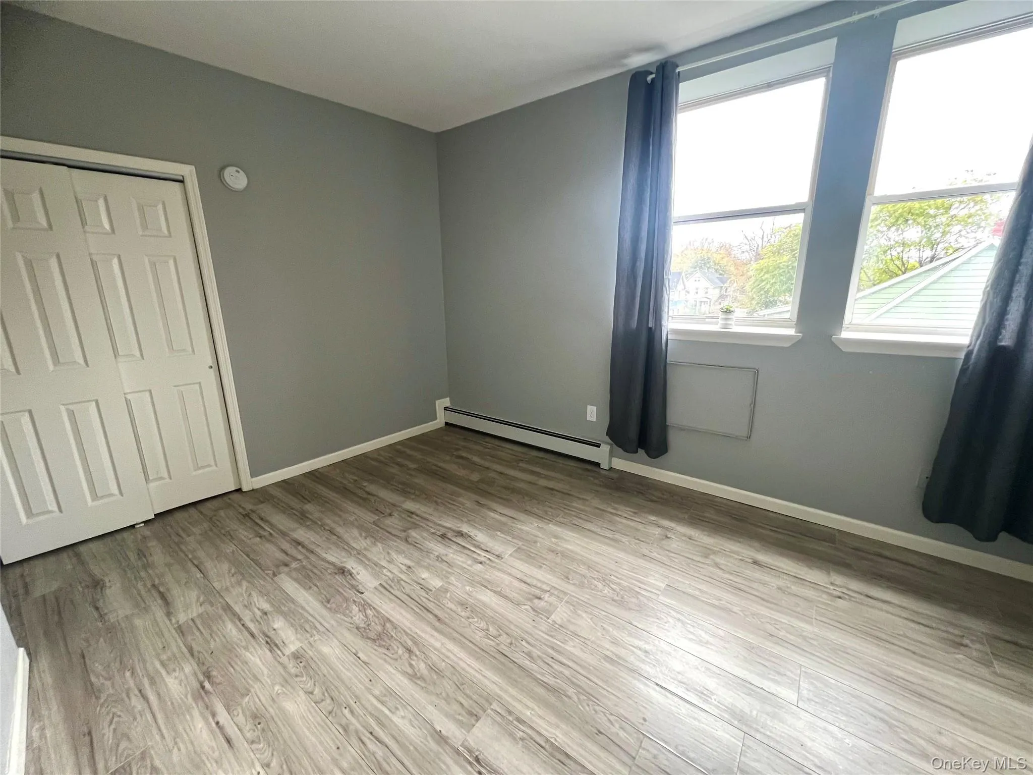Unfurnished bedroom featuring light wood finished floors, a baseboard heating unit, and a closet Unfurnished bedroom featuring light wood finished floors, a baseboard heating unit, and a closet