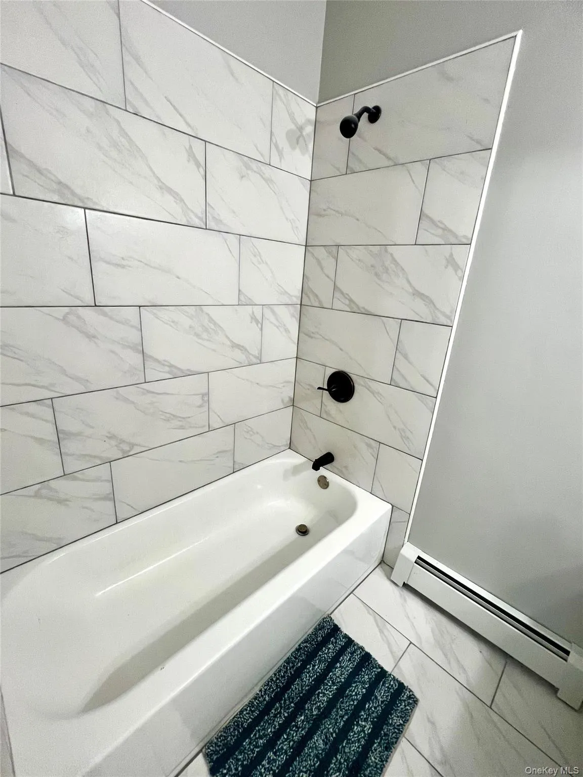 Bathroom with a baseboard radiator, washtub / shower combination, and marble finish flooring Bathroom with a baseboard radiator, washtub / shower combination, and marble finish flooring