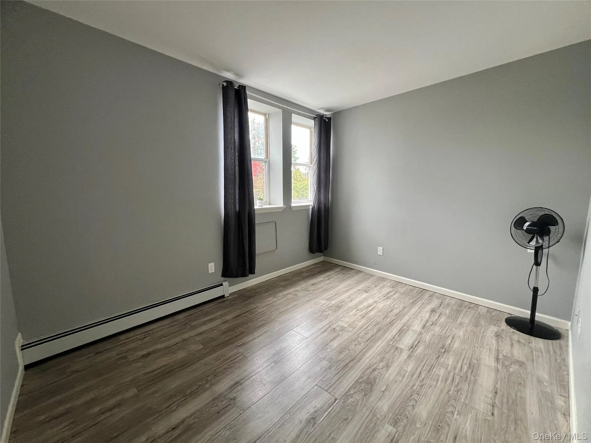 Unfurnished room with baseboard heating and wood finished floors Unfurnished room with baseboard heating and wood finished floors