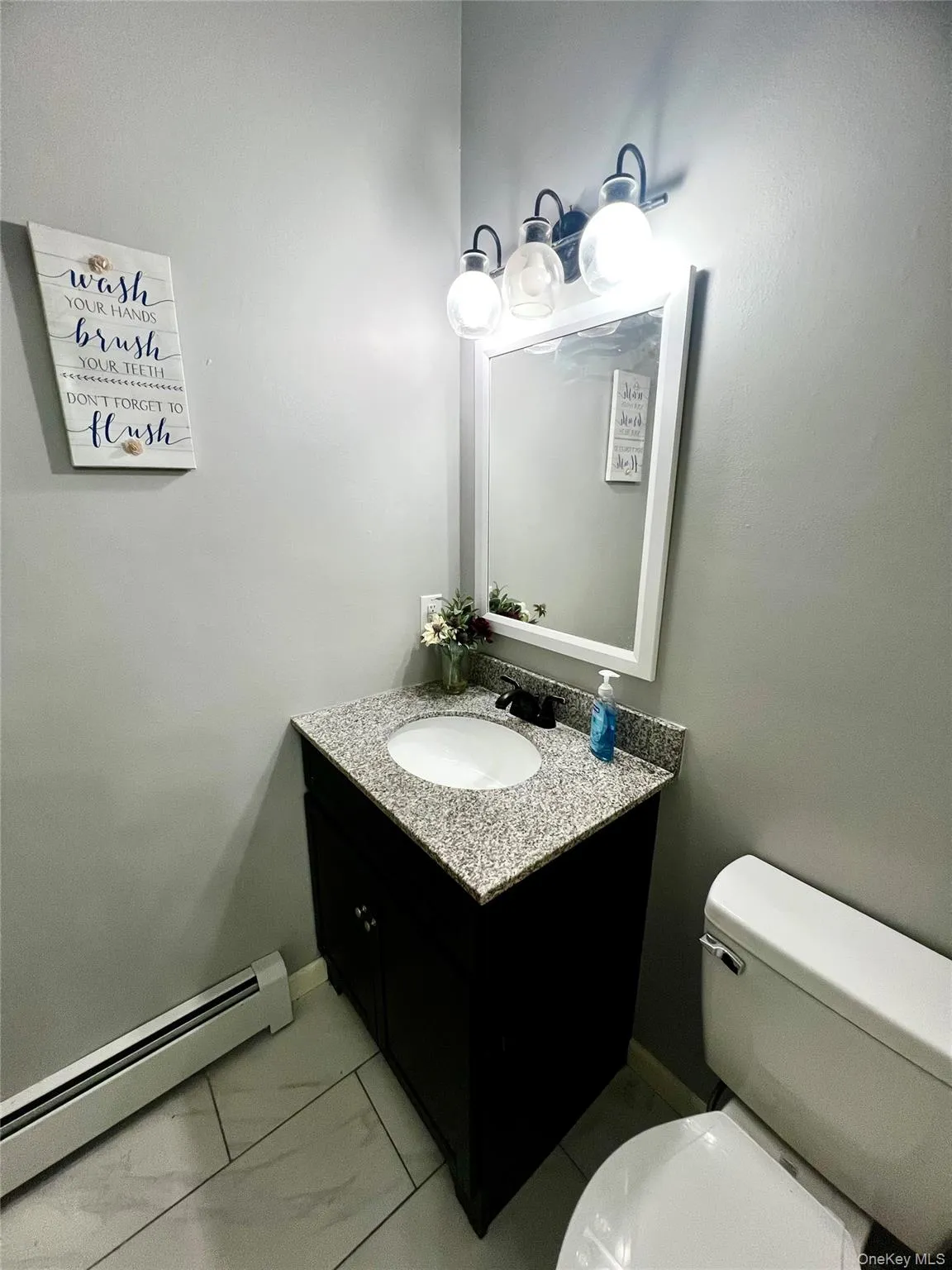 Half bathroom with a baseboard heating unit, vanity, and light marble finish flooring Half bathroom with a baseboard heating unit, vanity, and light marble finish flooring