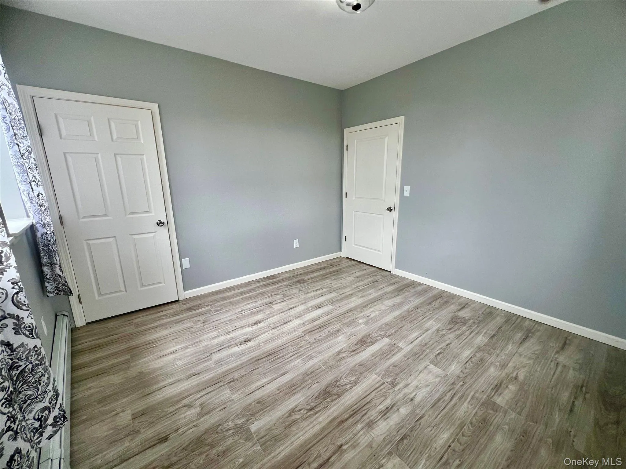 Unfurnished bedroom with light wood finished floors and baseboard heating Unfurnished bedroom with light wood finished floors and baseboard heating
