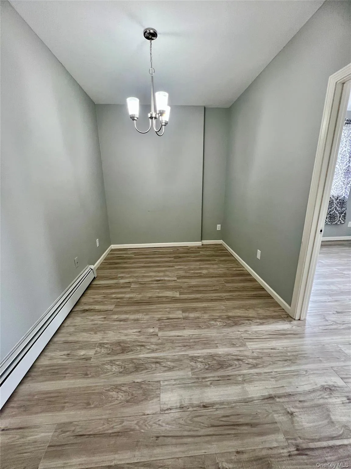 Empty room with a baseboard heating unit, light wood-type flooring, and a chandelier Empty room with a baseboard heating unit, light wood-type flooring, and a chandelier