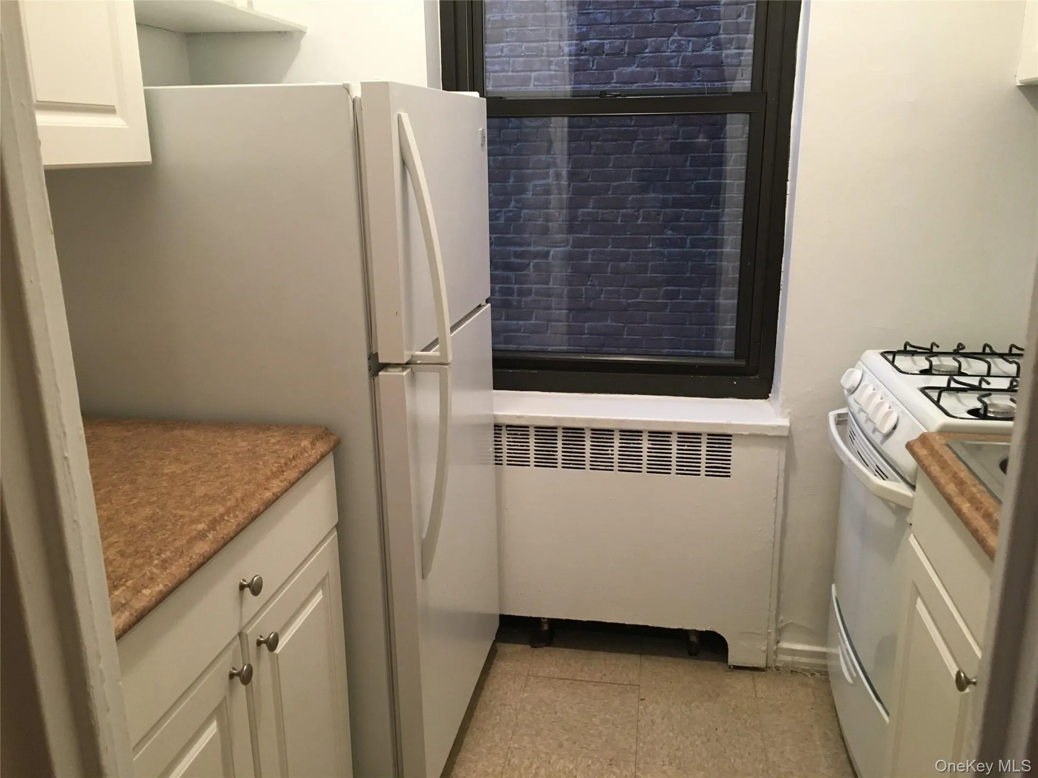 Kitchen with white cabinetry, white appliances, and radiator Kitchen with white cabinetry, white appliances, and radiator