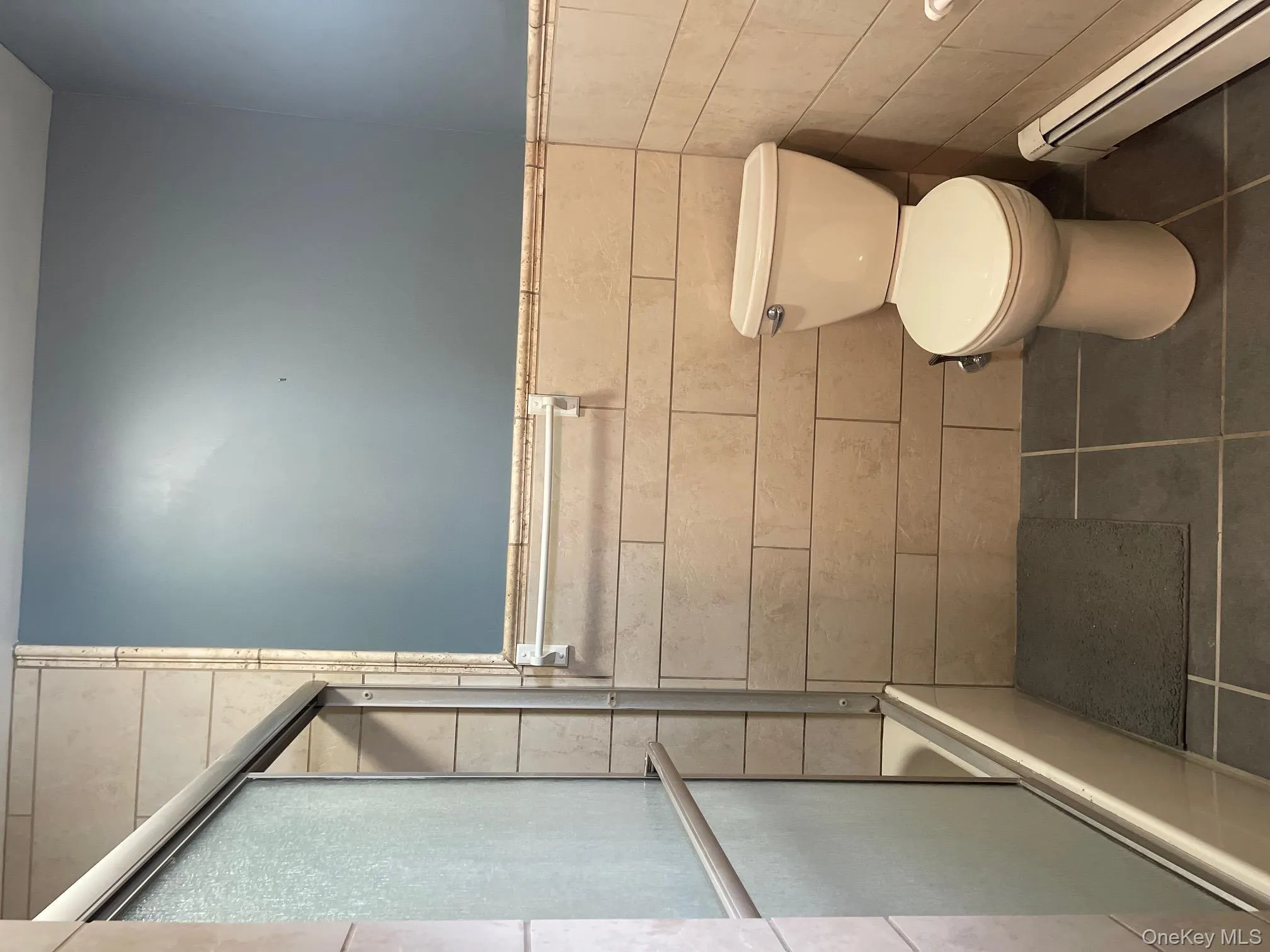 Full bath with a baseboard radiator, dark tile patterned flooring, tile walls, enclosed tub / shower combo, and wainscoting Full bath with a baseboard radiator, dark tile patterned flooring, tile walls, enclosed tub / shower combo, and wainscoting