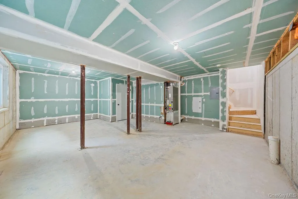 Unfinished below grade area featuring heating unit, stairs, and electric panel Unfinished below grade area featuring heating unit, stairs, and electric panel