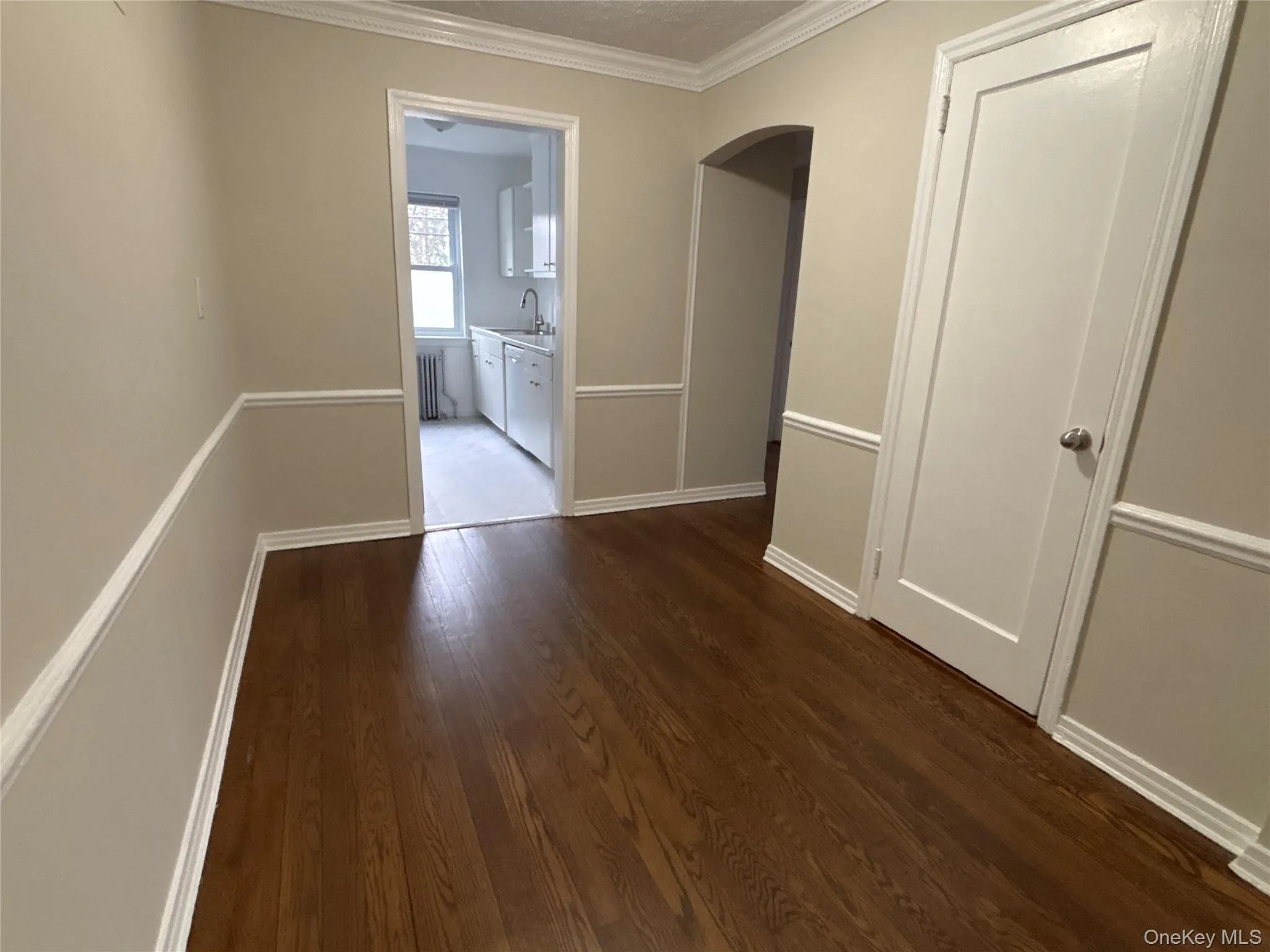 Corridor with crown molding, arched walkways, dark wood-style floors, and radiator Corridor with crown molding, arched walkways, dark wood-style floors, and radiator