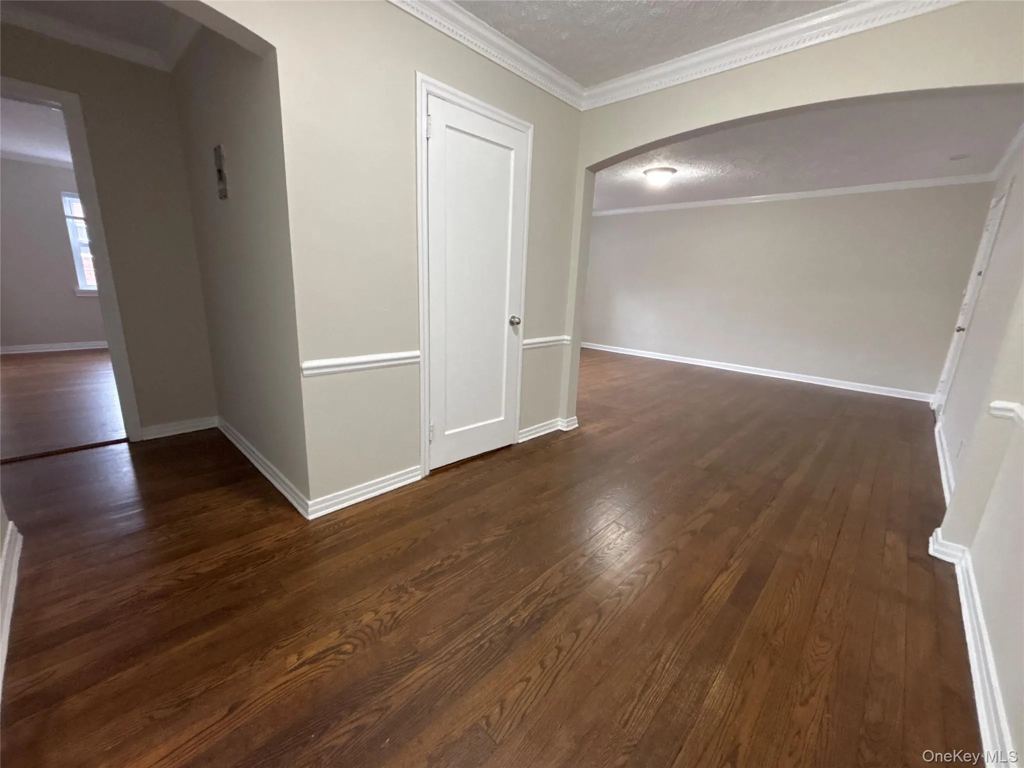 Empty room featuring arched walkways, crown molding, dark wood-style floors, and a textured ceiling Empty room featuring arched walkways, crown molding, dark wood-style floors, and a textured ceiling