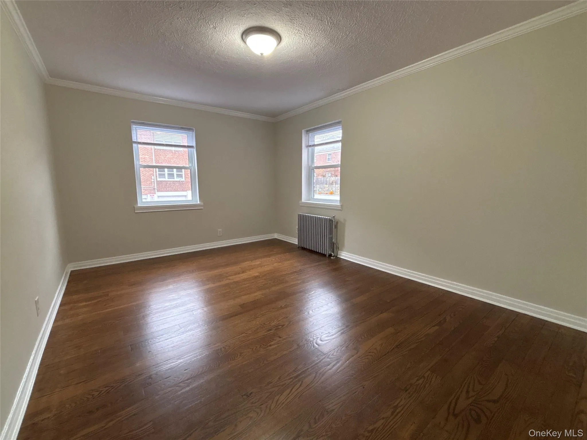Empty room with a textured ceiling, dark wood-style flooring, radiator, and ornamental molding Empty room with a textured ceiling, dark wood-style flooring, radiator, and ornamental molding
