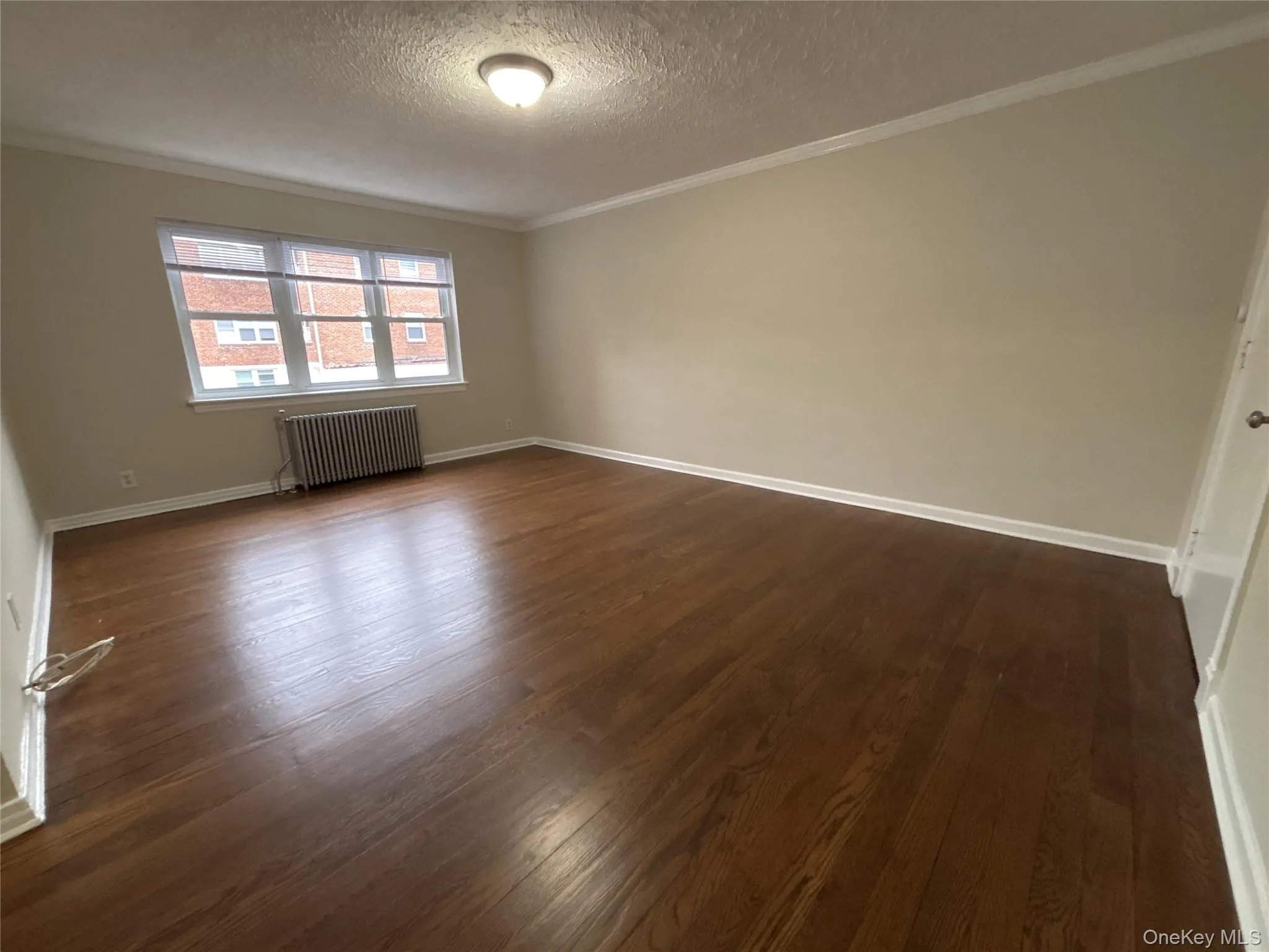 Unfurnished room with radiator heating unit, a textured ceiling, crown molding, and dark wood-type flooring Unfurnished room with radiator heating unit, a textured ceiling, crown molding, and dark wood-type flooring