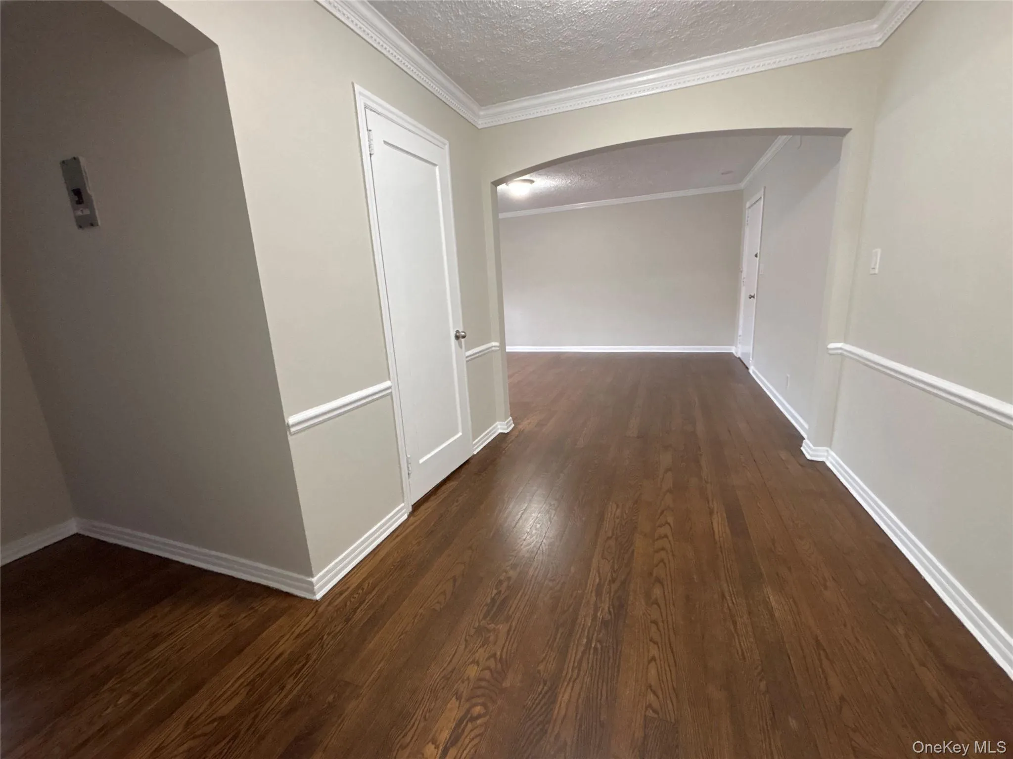 Hall with arched walkways, a textured ceiling, dark wood-type flooring, and crown molding Hall with arched walkways, a textured ceiling, dark wood-type flooring, and crown molding