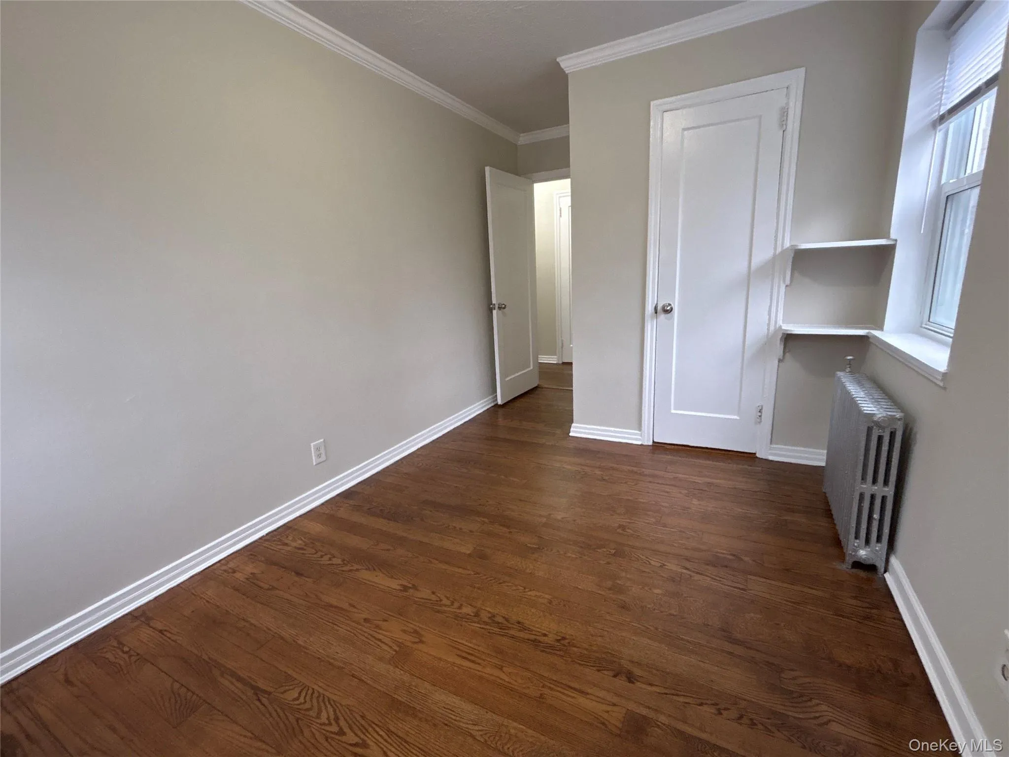 Unfurnished bedroom featuring ornamental molding, radiator heating unit, and dark wood-style floors Unfurnished bedroom featuring ornamental molding, radiator heating unit, and dark wood-style floors
