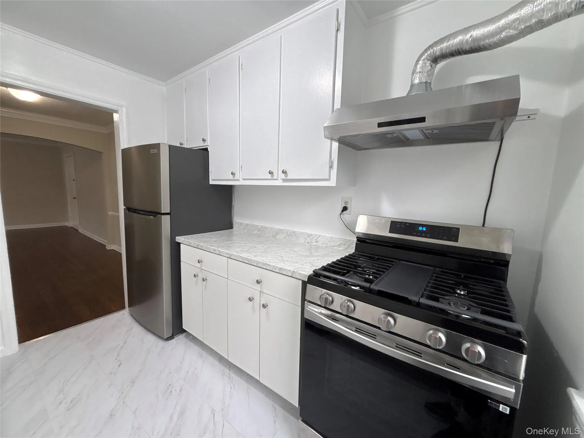 Kitchen with appliances with stainless steel finishes, light marble finish flooring, crown molding, white cabinetry, and exhaust hood Kitchen with appliances with stainless steel finishes, light marble finish flooring, crown molding, white cabinetry, and exhaust hood