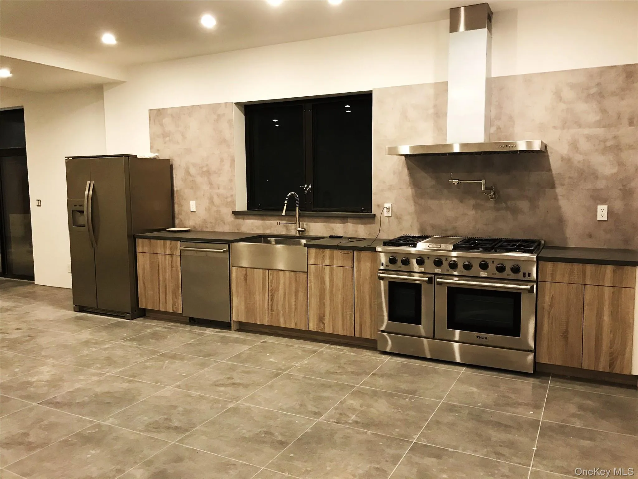 Kitchen featuring wall chimney range hood, appliances with stainless steel finishes, recessed lighting, decorative backsplash, and brown cabinetry Kitchen featuring wall chimney range hood, appliances with stainless steel finishes, recessed lighting, decorative backsplash, and brown cabinetry