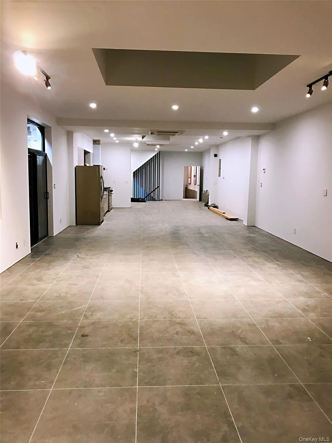 Basement featuring rail lighting, freestanding refrigerator, light tile patterned floors, and recessed lighting Basement featuring rail lighting, freestanding refrigerator, light tile patterned floors, and recessed lighting