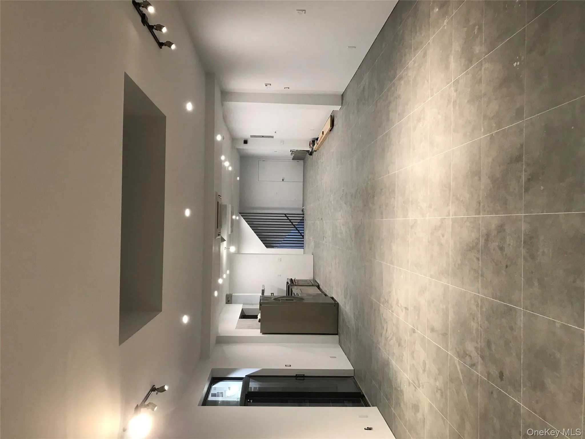 Basement featuring track lighting, refrigerator, and light tile patterned flooring Basement featuring track lighting, refrigerator, and light tile patterned flooring