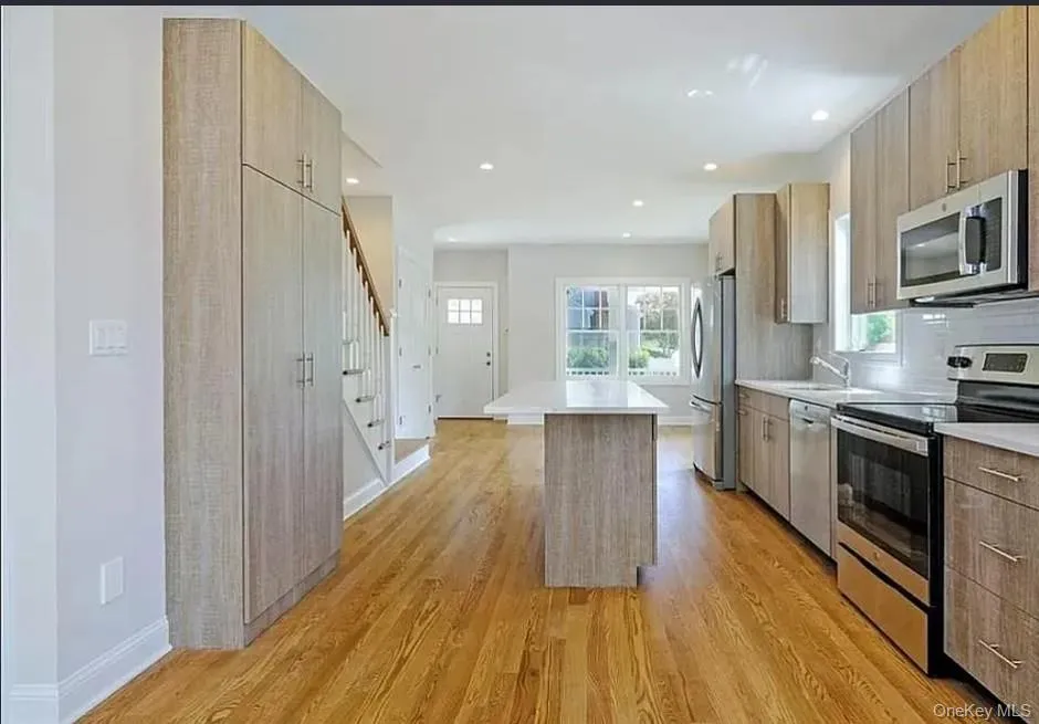 Kitchen with stainless steel appliances, a center island, modern cabinets, light countertops, and light wood finished floors Kitchen with stainless steel appliances, a center island, modern cabinets, light countertops, and light wood finished floors