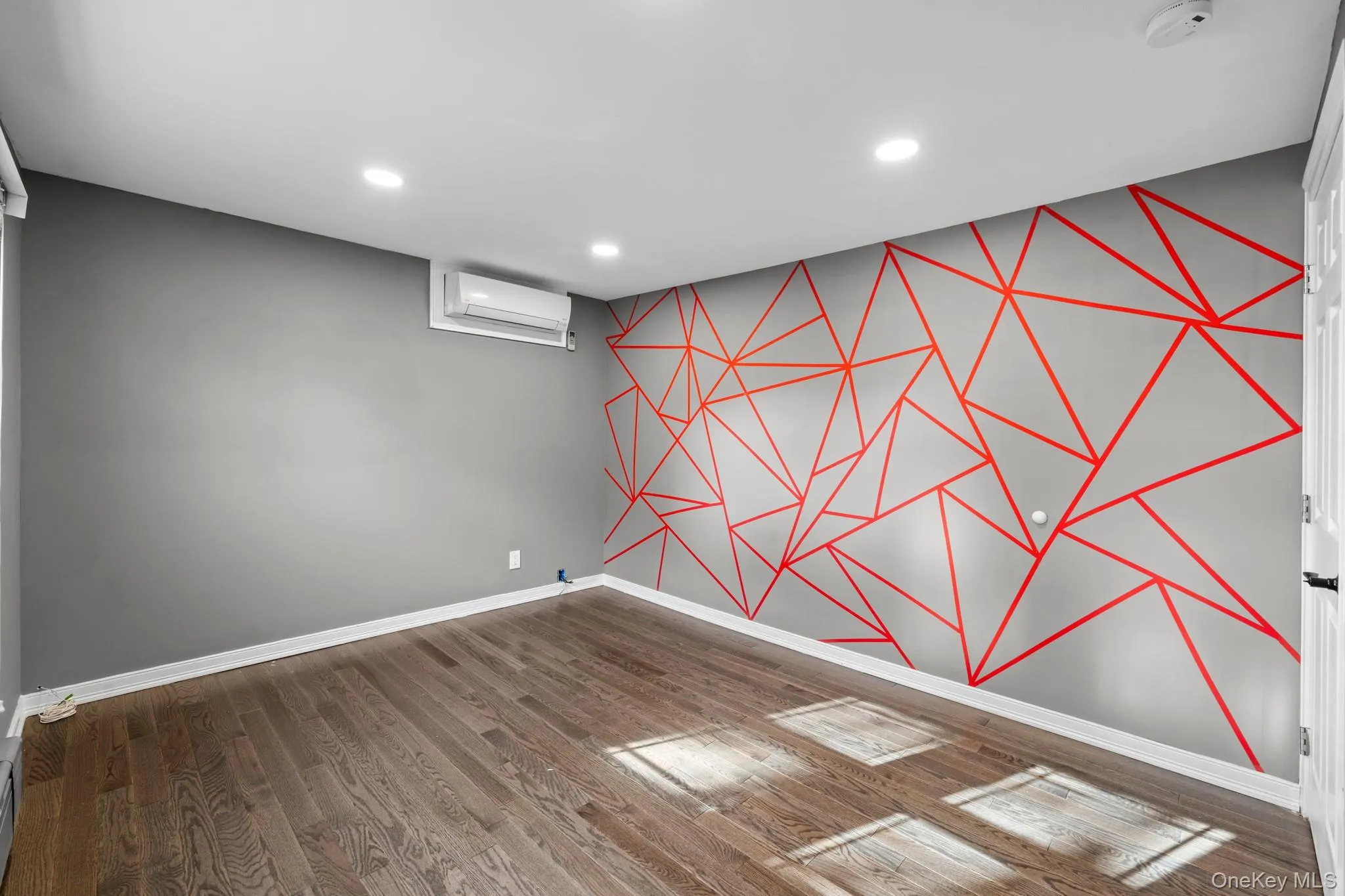 Finished basement with an accent wall, recessed lighting, wood finished floors, wallpapered walls, and an AC wall unit Finished basement with an accent wall, recessed lighting, wood finished floors, wallpapered walls, and an AC wall unit