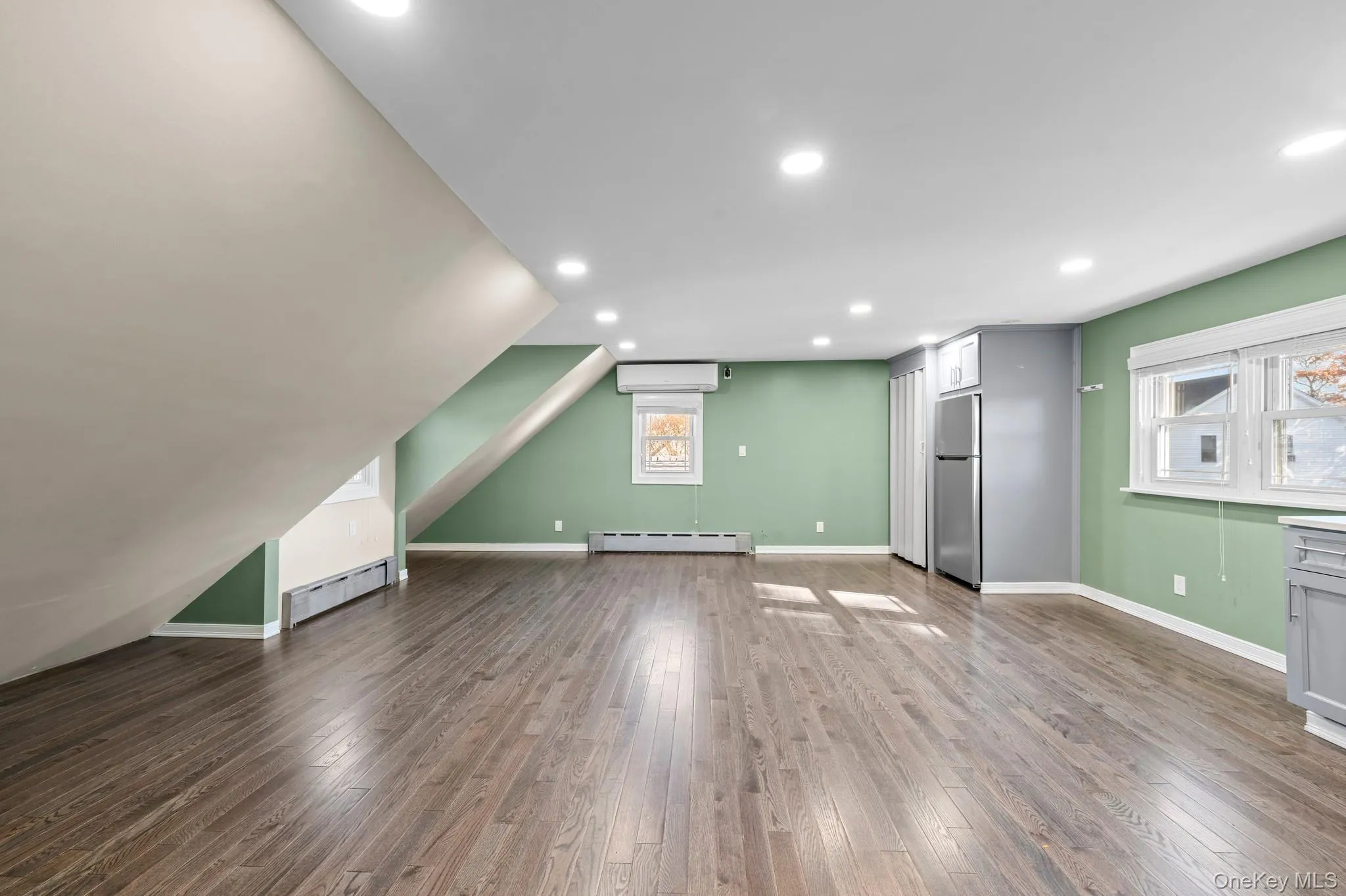 Additional living space featuring dark wood-style flooring, recessed lighting, baseboard heating, and a wall mounted air conditioner Additional living space featuring dark wood-style flooring, recessed lighting, baseboard heating, and a wall mounted air conditioner