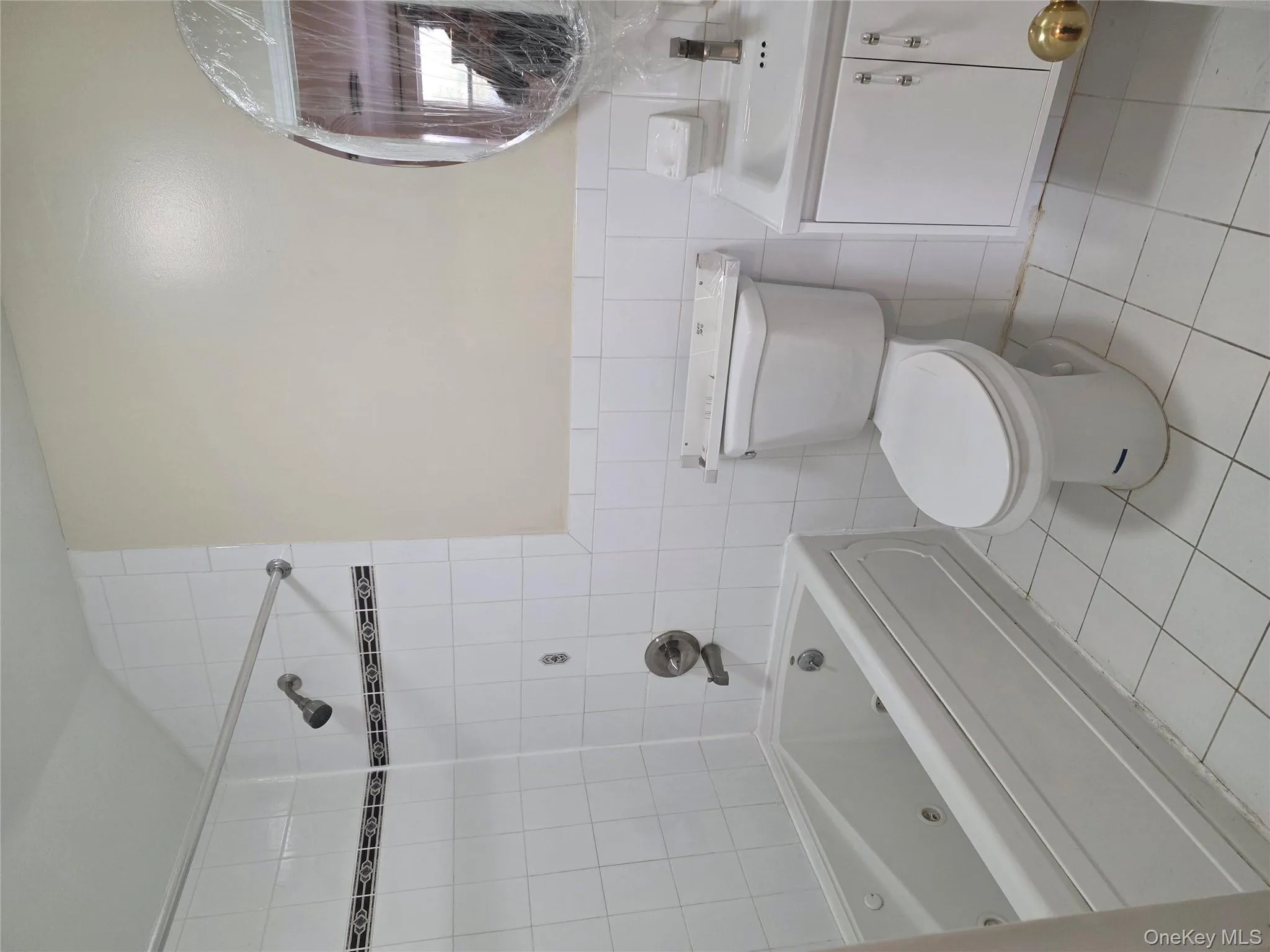 Full bath featuring tile walls, light tile patterned flooring, a combined bath / shower with jetted tub, vanity, and wainscoting Full bath featuring tile walls, light tile patterned flooring, a combined bath / shower with jetted tub, vanity, and wainscoting