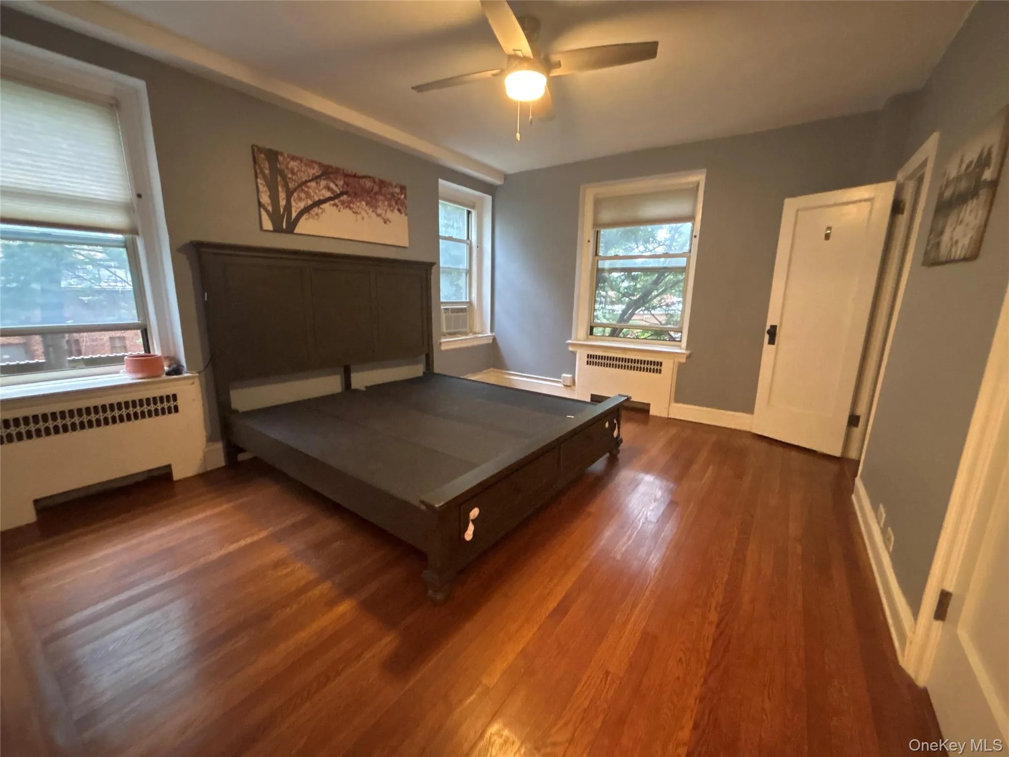 Bedroom with radiator heating unit, dark wood-style flooring, and a ceiling fan Bedroom with radiator heating unit, dark wood-style flooring, and a ceiling fan