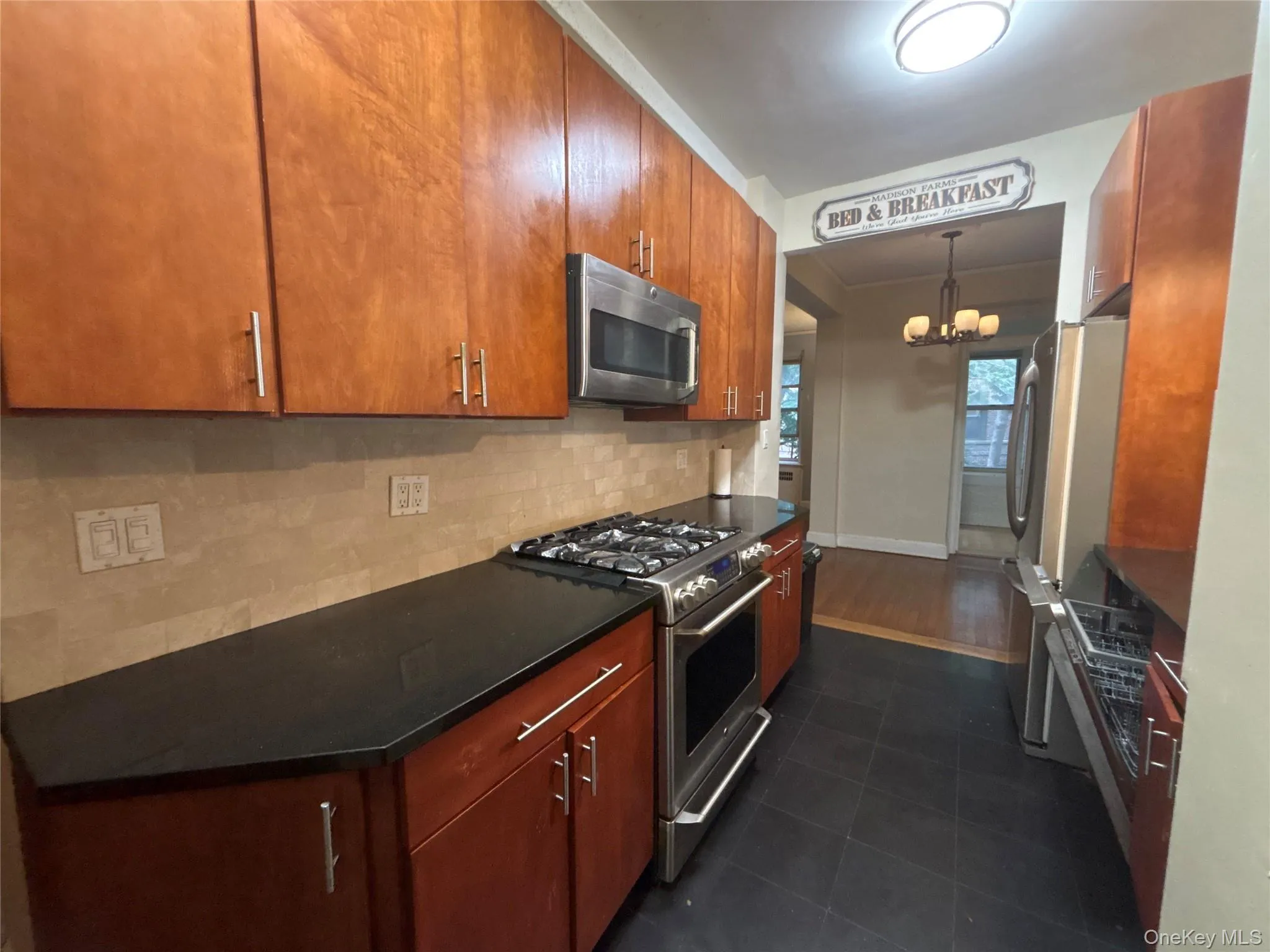 Kitchen with tasteful backsplash, appliances with stainless steel finishes, a chandelier, pendant lighting, and brown cabinets Kitchen with tasteful backsplash, appliances with stainless steel finishes, a chandelier, pendant lighting, and brown cabinets