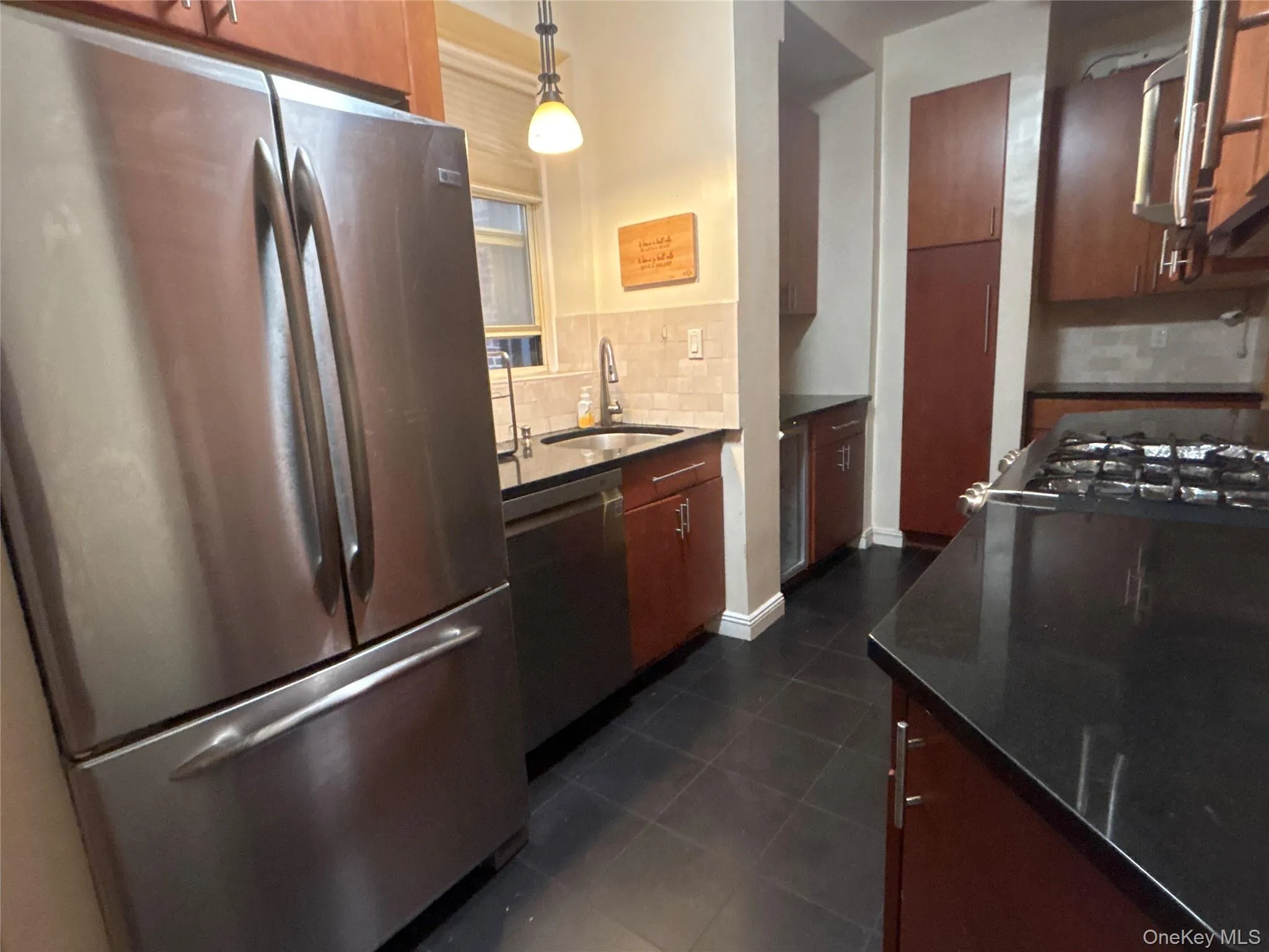 Kitchen with appliances with stainless steel finishes, tasteful backsplash, dark stone counters, dark tile patterned floors, and pendant lighting Kitchen with appliances with stainless steel finishes, tasteful backsplash, dark stone counters, dark tile patterned floors, and pendant lighting