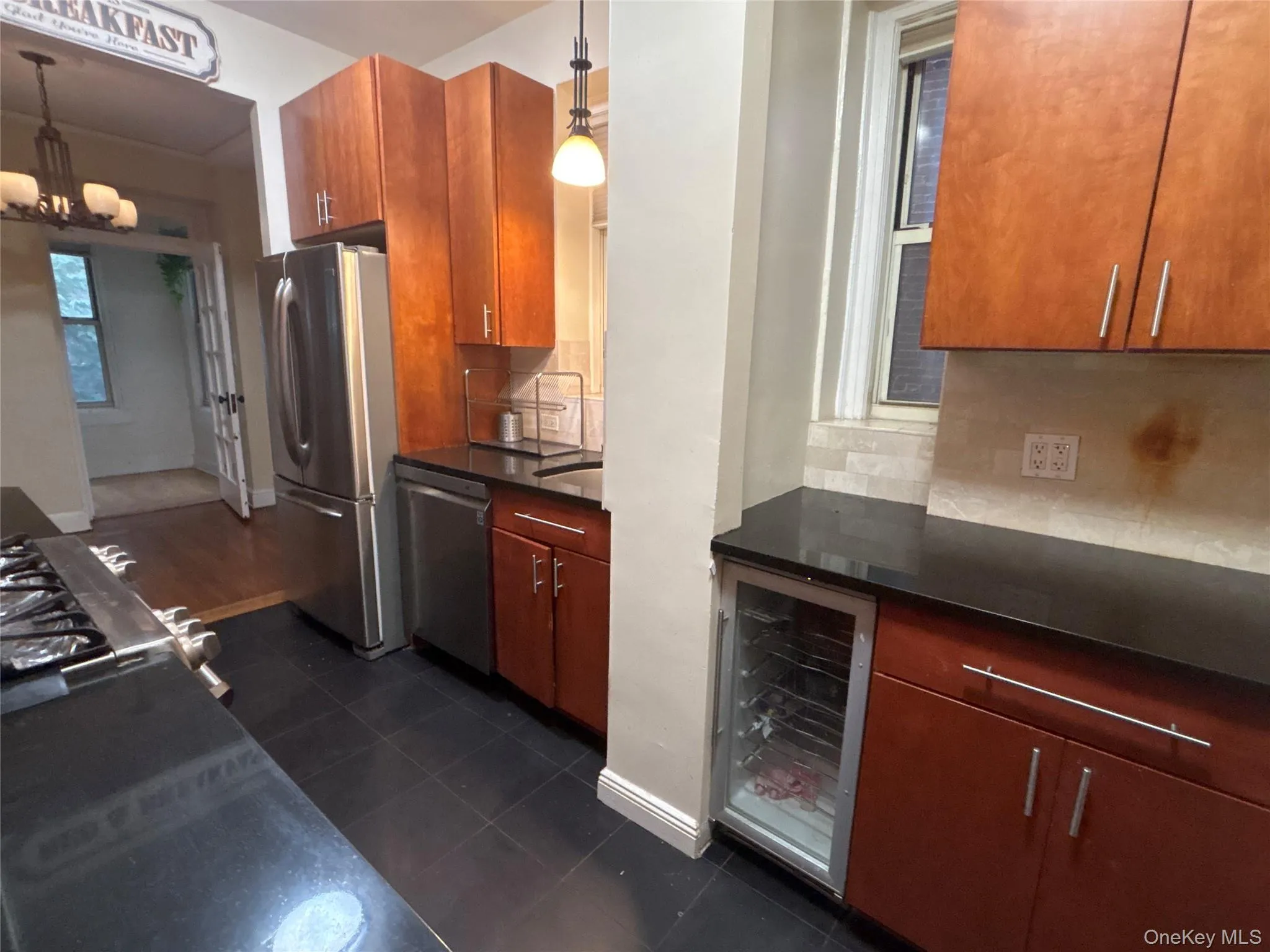 Kitchen featuring appliances with stainless steel finishes, beverage cooler, hanging light fixtures, dark tile patterned floors, and backsplash Kitchen featuring appliances with stainless steel finishes, beverage cooler, hanging light fixtures, dark tile patterned floors, and backsplash