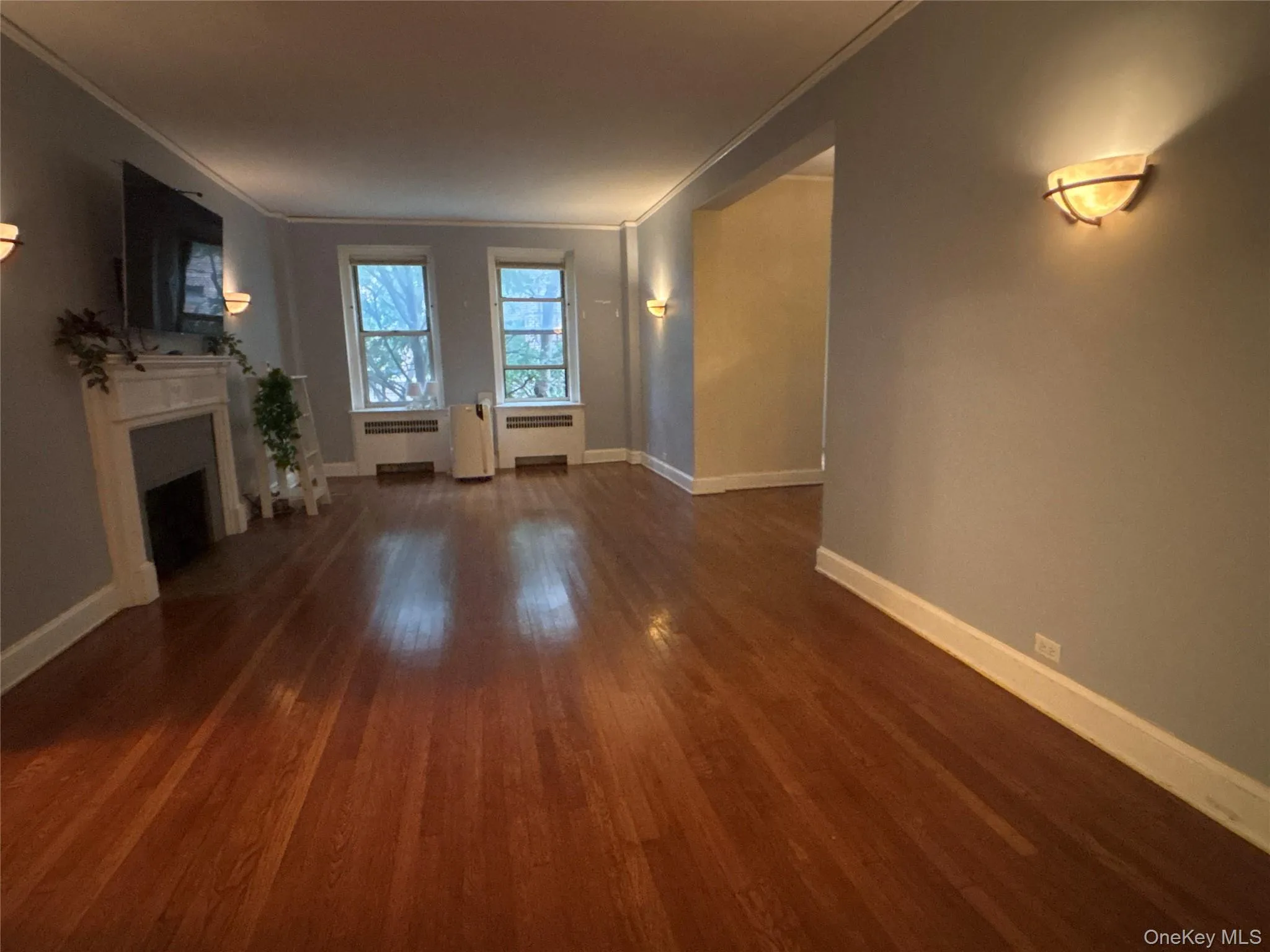 Unfurnished living room featuring dark wood-type flooring, a fireplace, ornamental molding, and radiator heating unit Unfurnished living room featuring dark wood-type flooring, a fireplace, ornamental molding, and radiator heating unit