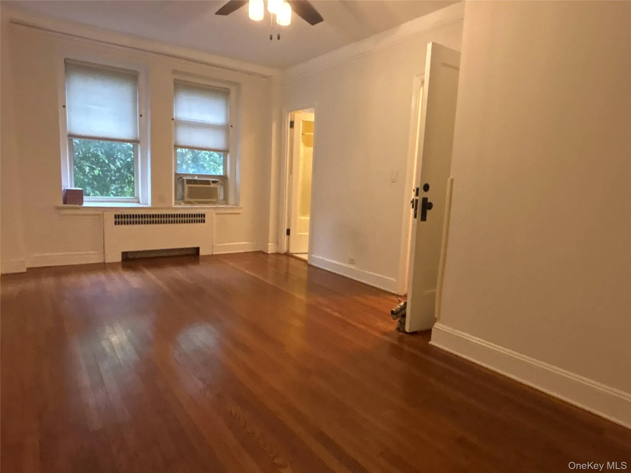Spare room with radiator heating unit, dark wood-type flooring, crown molding, ceiling fan, and cooling unit Spare room with radiator heating unit, dark wood-type flooring, crown molding, ceiling fan, and cooling unit