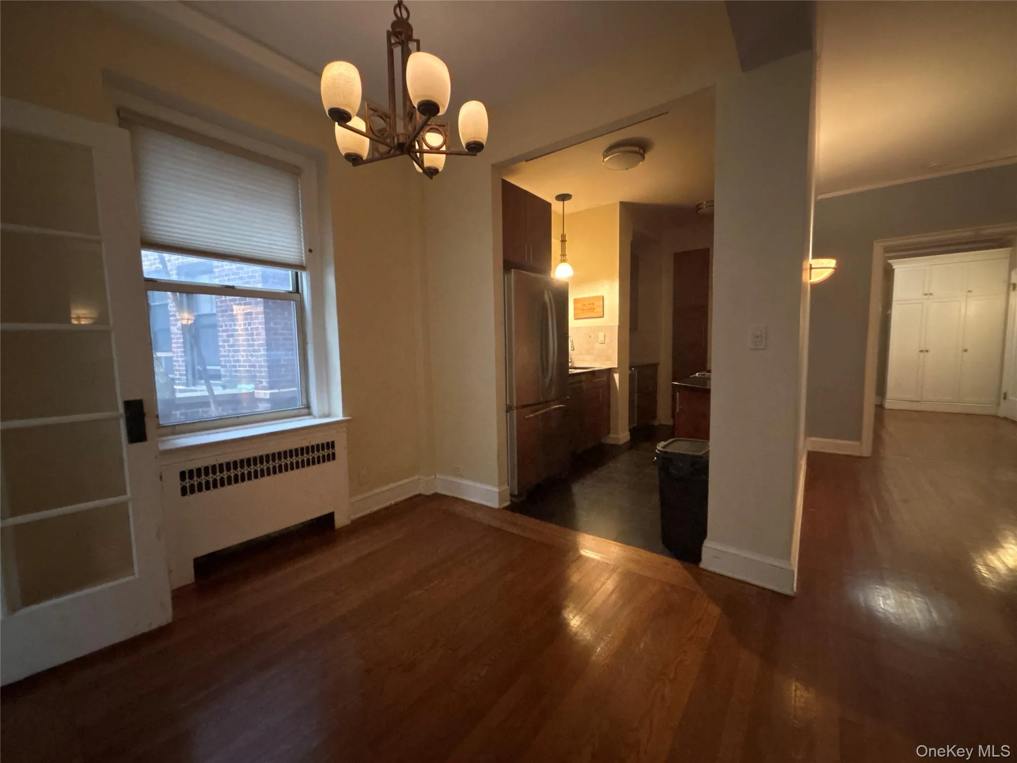 Unfurnished dining area featuring radiator heating unit, dark wood-type flooring, and a chandelier Unfurnished dining area featuring radiator heating unit, dark wood-type flooring, and a chandelier
