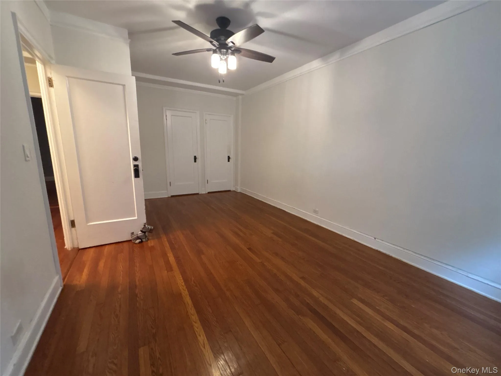 Unfurnished bedroom featuring dark wood-style floors, ornamental molding, a ceiling fan, and multiple closets Unfurnished bedroom featuring dark wood-style floors, ornamental molding, a ceiling fan, and multiple closets