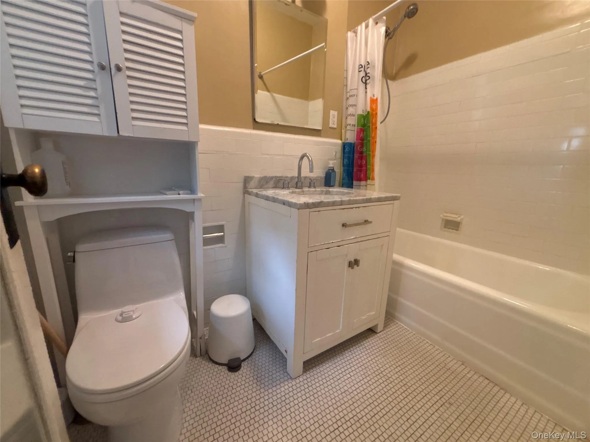 Bathroom featuring tile walls, shower / bath combo, vanity, a wainscoted wall, and light tile patterned flooring Bathroom featuring tile walls, shower / bath combo, vanity, a wainscoted wall, and light tile patterned flooring