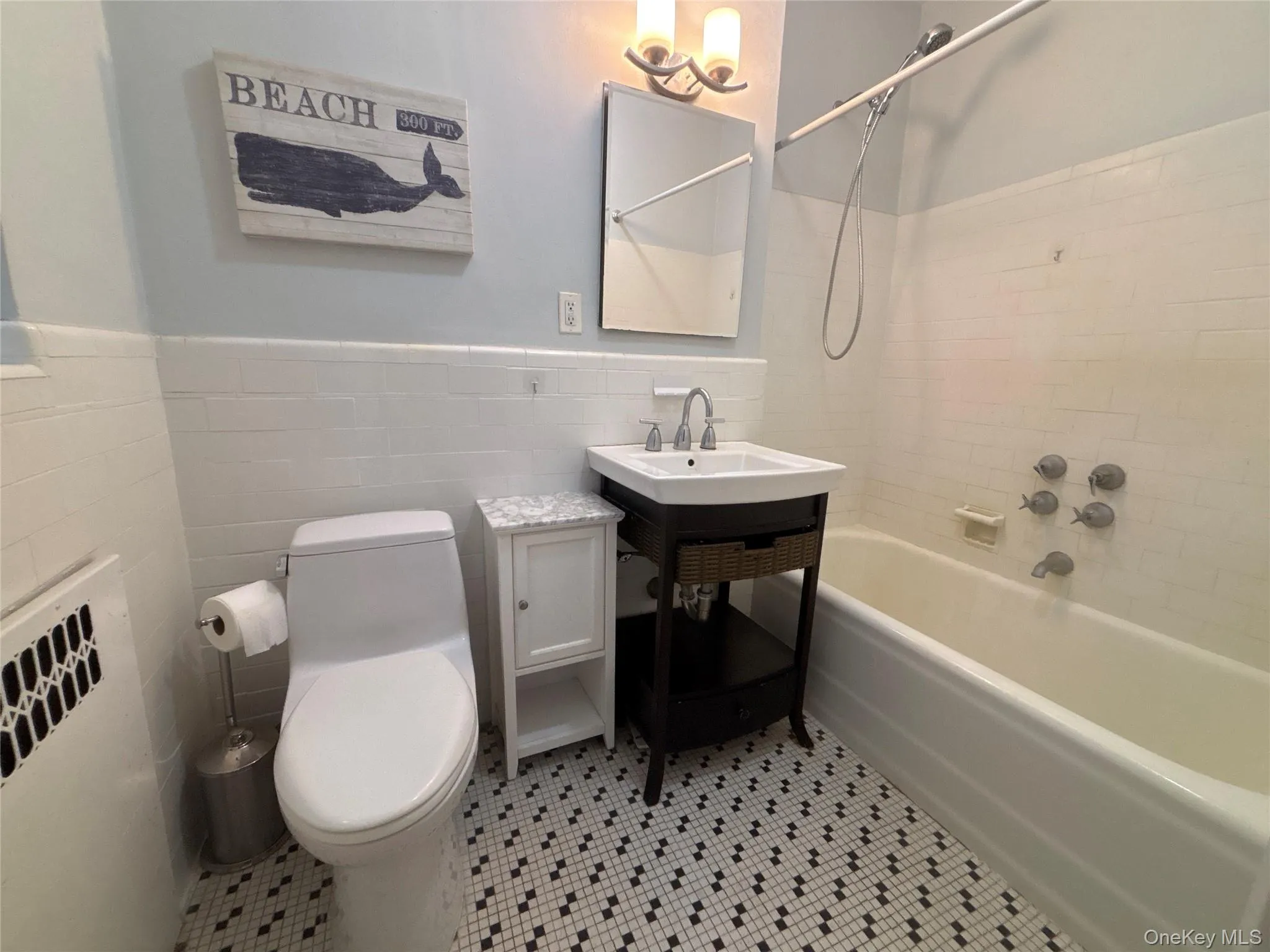 Bathroom with washtub / shower combination, light tile patterned floors, tile walls, vanity, and wainscoting Bathroom with washtub / shower combination, light tile patterned floors, tile walls, vanity, and wainscoting