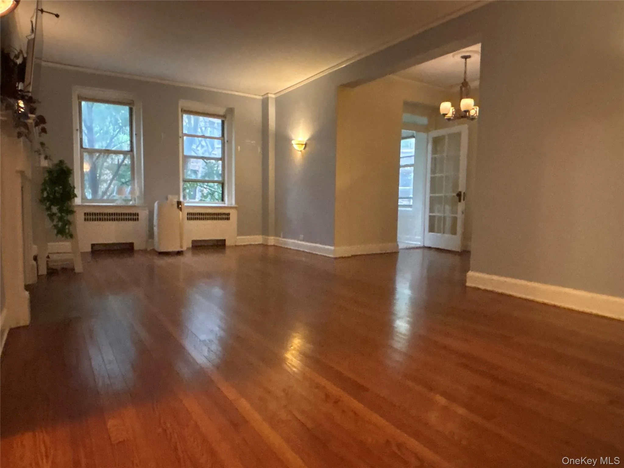 Unfurnished living room featuring healthy amount of natural light, dark wood-style floors, radiator heating unit, a chandelier, and ornamental molding Unfurnished living room featuring healthy amount of natural light, dark wood-style floors, radiator heating unit, a chandelier, and ornamental molding