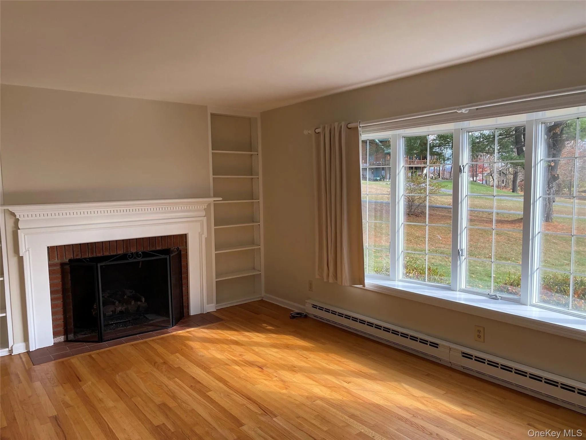 Living room with window seat area, light wood-style floors, a brick fireplace, and built in shelves Living room with window seat area, light wood-style floors, a brick fireplace, and built in shelves