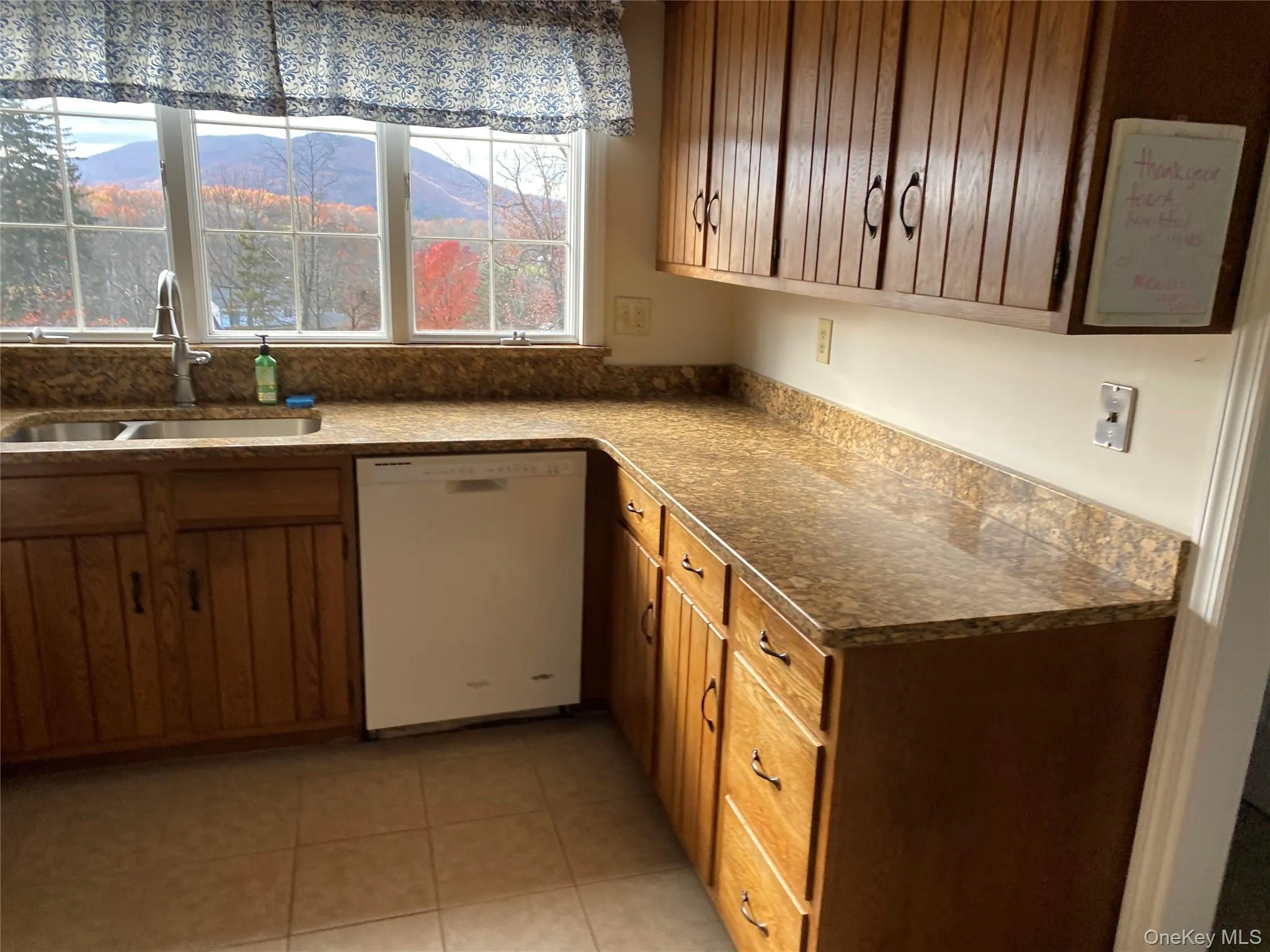 Kitchen with dishwasher, light tile patterned flooring, a mountain view, dark countertops, and brown cabinets Kitchen with dishwasher, light tile patterned flooring, a mountain view, dark countertops, and brown cabinets