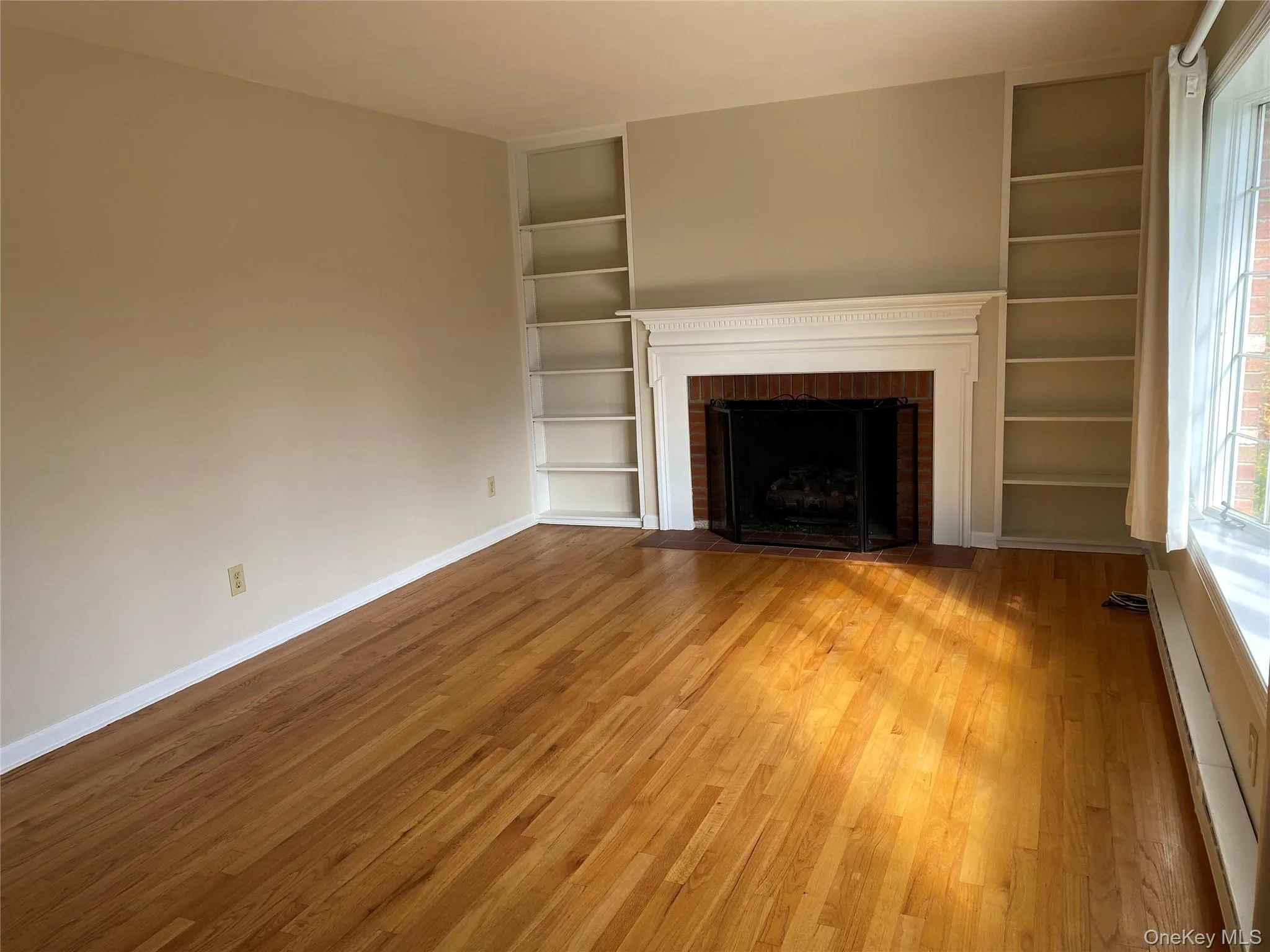 Living room with built in features, a baseboard radiator, hardwood floors, and a gas fireplace Living room with built in features, a baseboard radiator, hardwood floors, and a gas fireplace