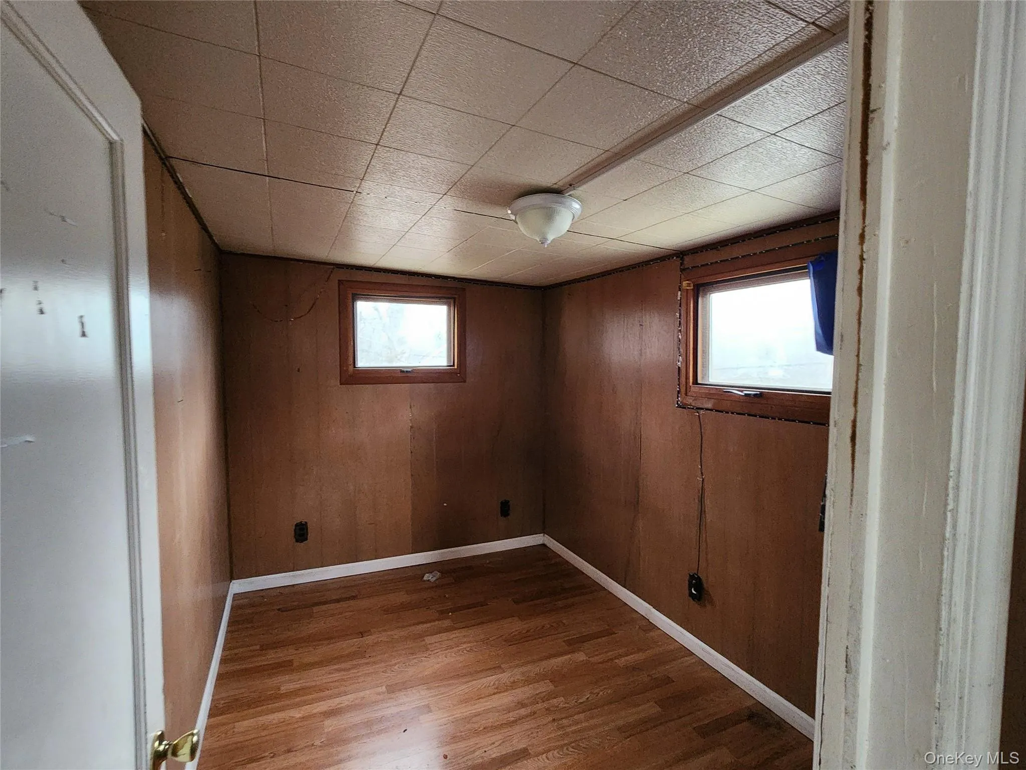Unfurnished room with wood walls, wood finished floors, and plenty of natural light Unfurnished room with wood walls, wood finished floors, and plenty of natural light