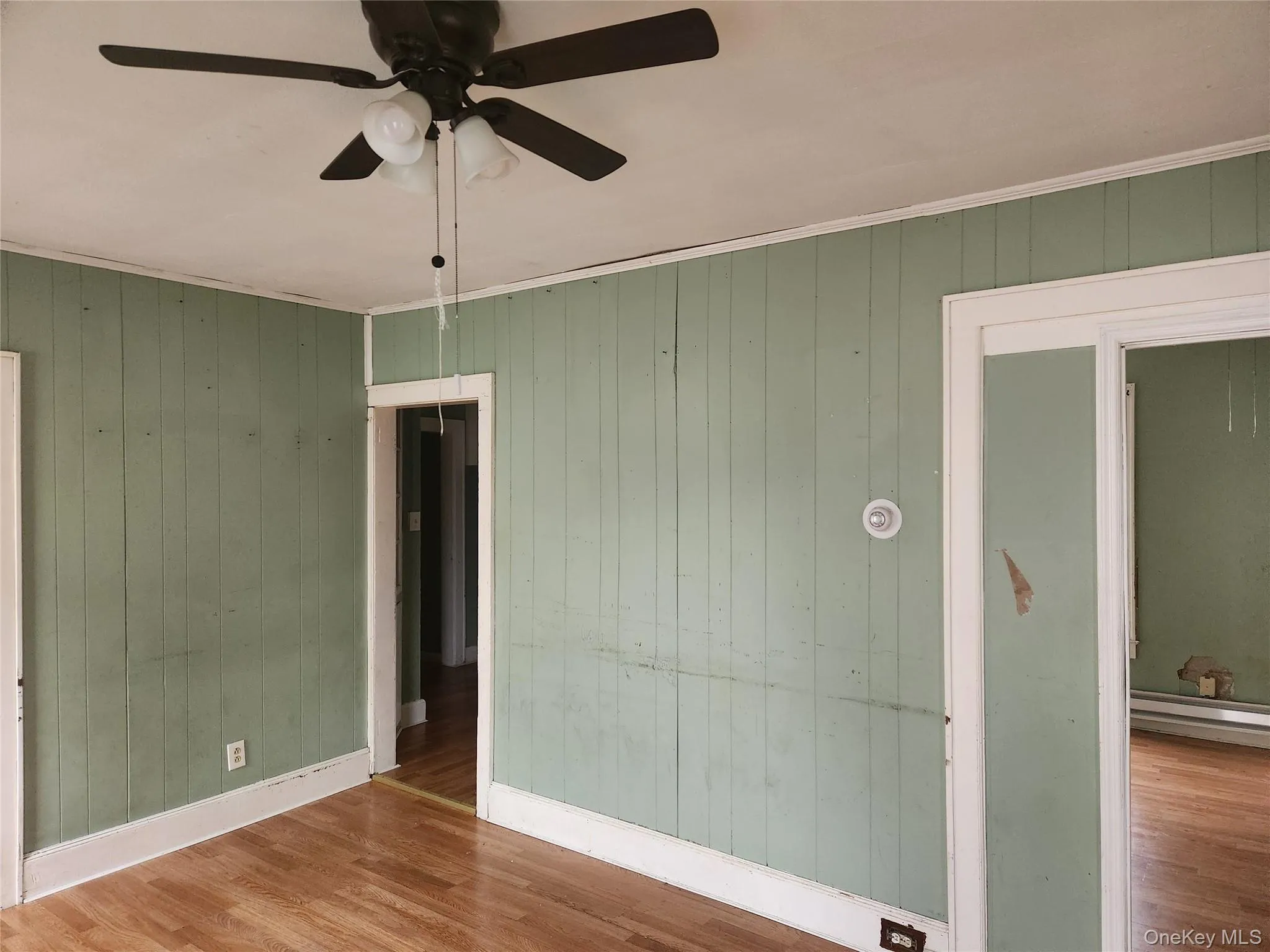 Unfurnished bedroom with wooden walls, wood finished floors, crown molding, and ceiling fan Unfurnished bedroom with wooden walls, wood finished floors, crown molding, and ceiling fan
