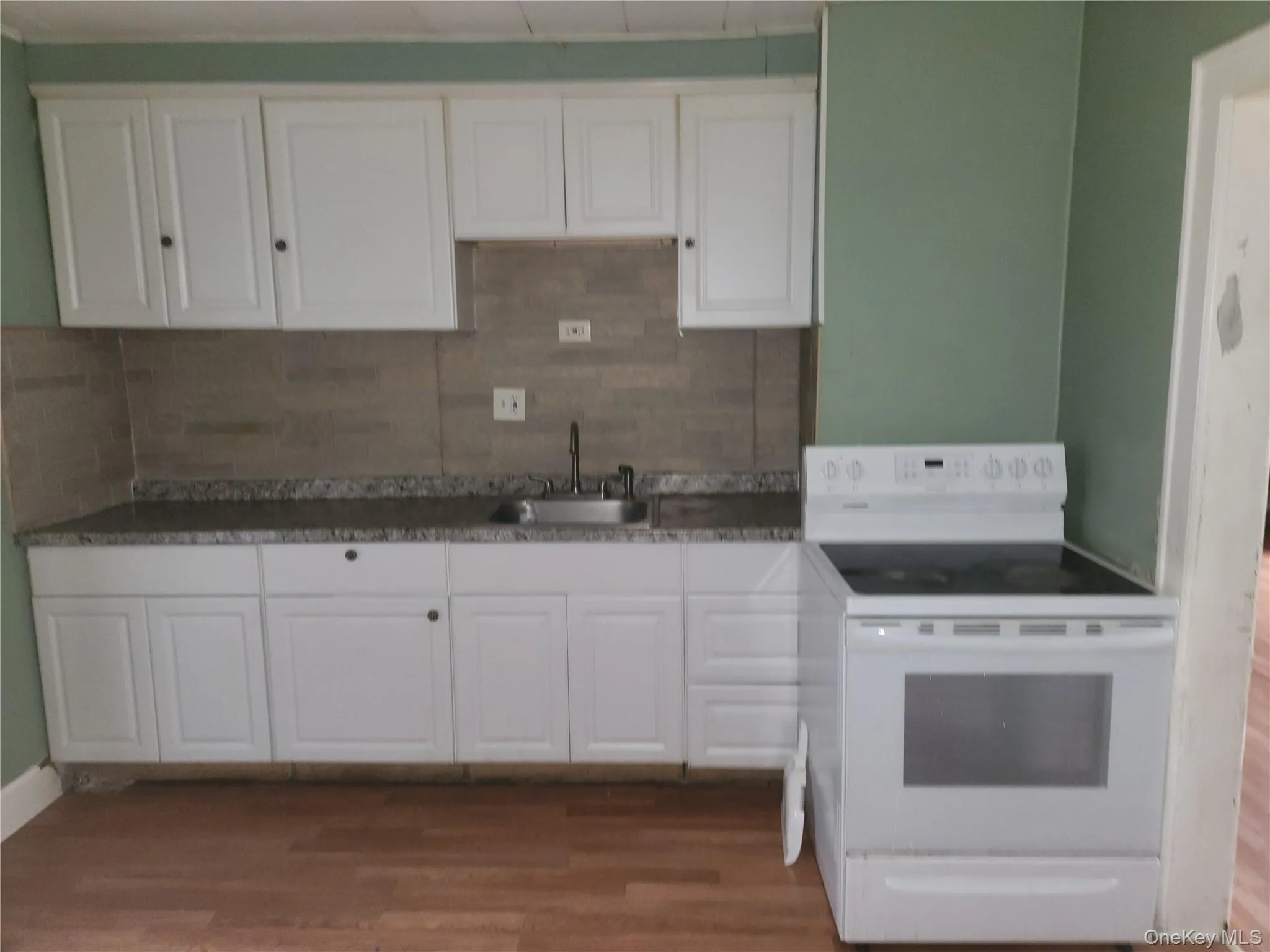 Kitchen featuring white electric range oven, white cabinetry, dark wood-style flooring, and decorative backsplash Kitchen featuring white electric range oven, white cabinetry, dark wood-style flooring, and decorative backsplash