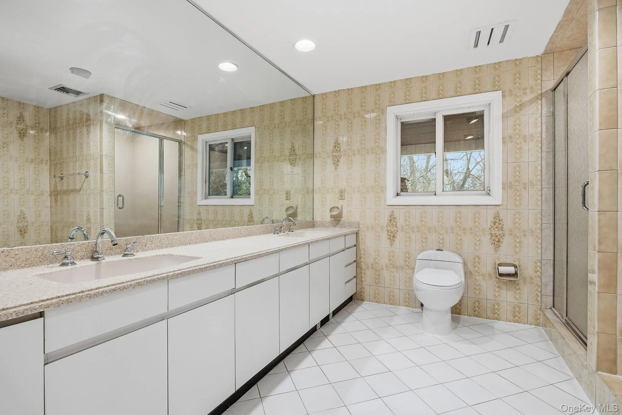 Full bath featuring double vanity, light tile patterned floors, a shower stall, tile walls, and recessed lighting Full bath featuring double vanity, light tile patterned floors, a shower stall, tile walls, and recessed lighting