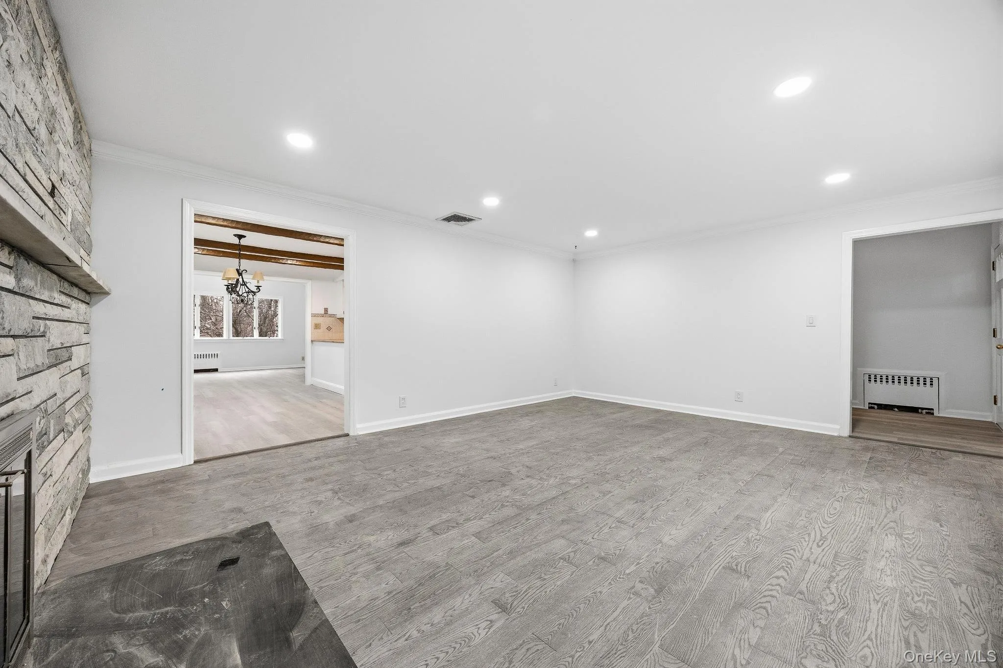 Unfurnished living room featuring light wood-style flooring, a fireplace, crown molding, radiator heating unit, and a chandelier Unfurnished living room featuring light wood-style flooring, a fireplace, crown molding, radiator heating unit, and a chandelier
